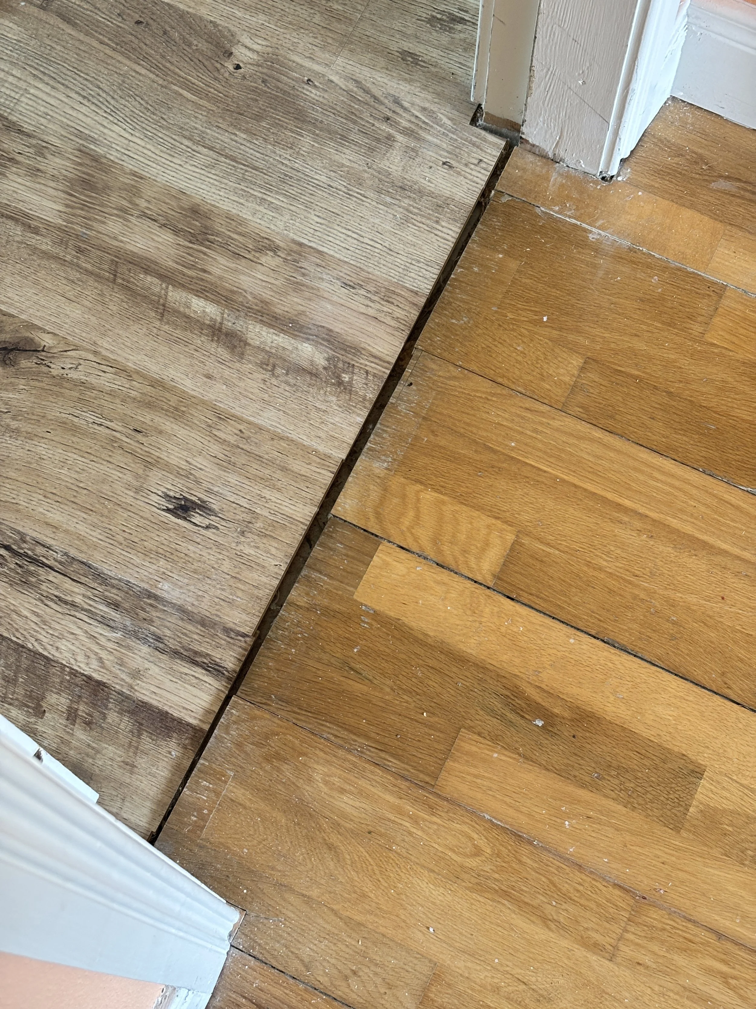 Doorway threshold between grey wood-effect laminate and oak floorboards with the saddle removed