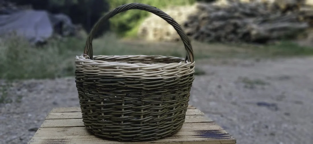 Woven basket with handle on wooden surface outdoors, blurry natural background.