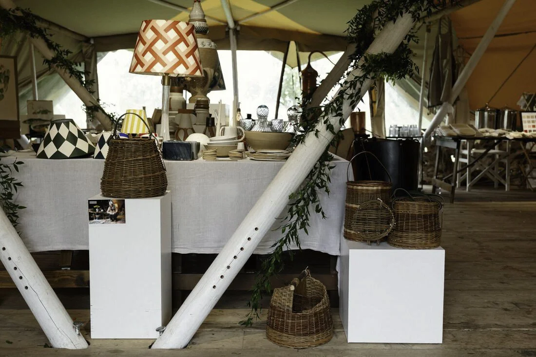 Display of woven baskets and tableware on a table inside a tent at a market or craft fair.