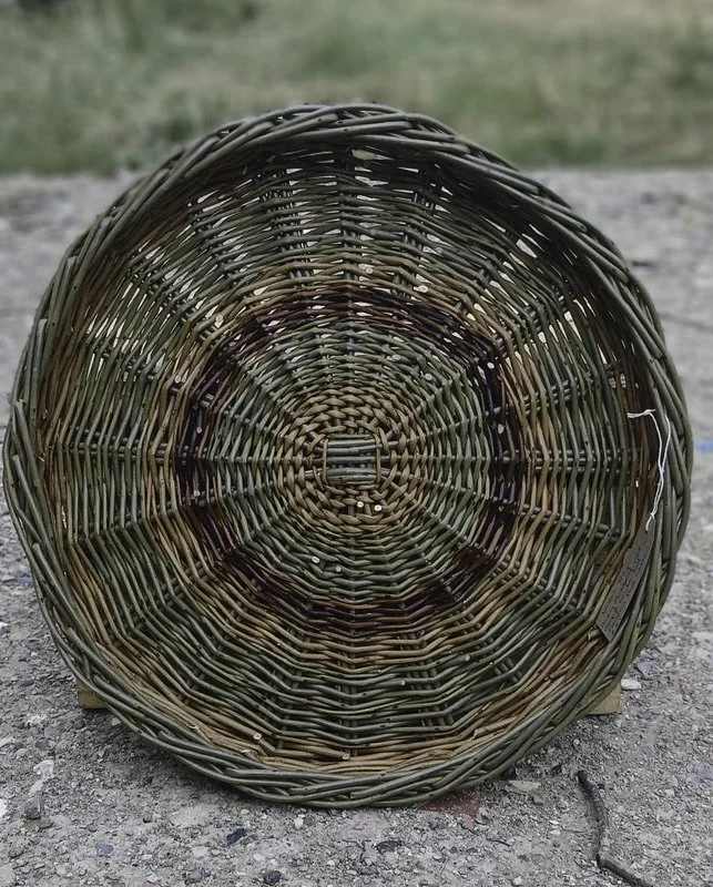 A round wicker basket placed on dirt ground outdoors, with a blurred grassy background.