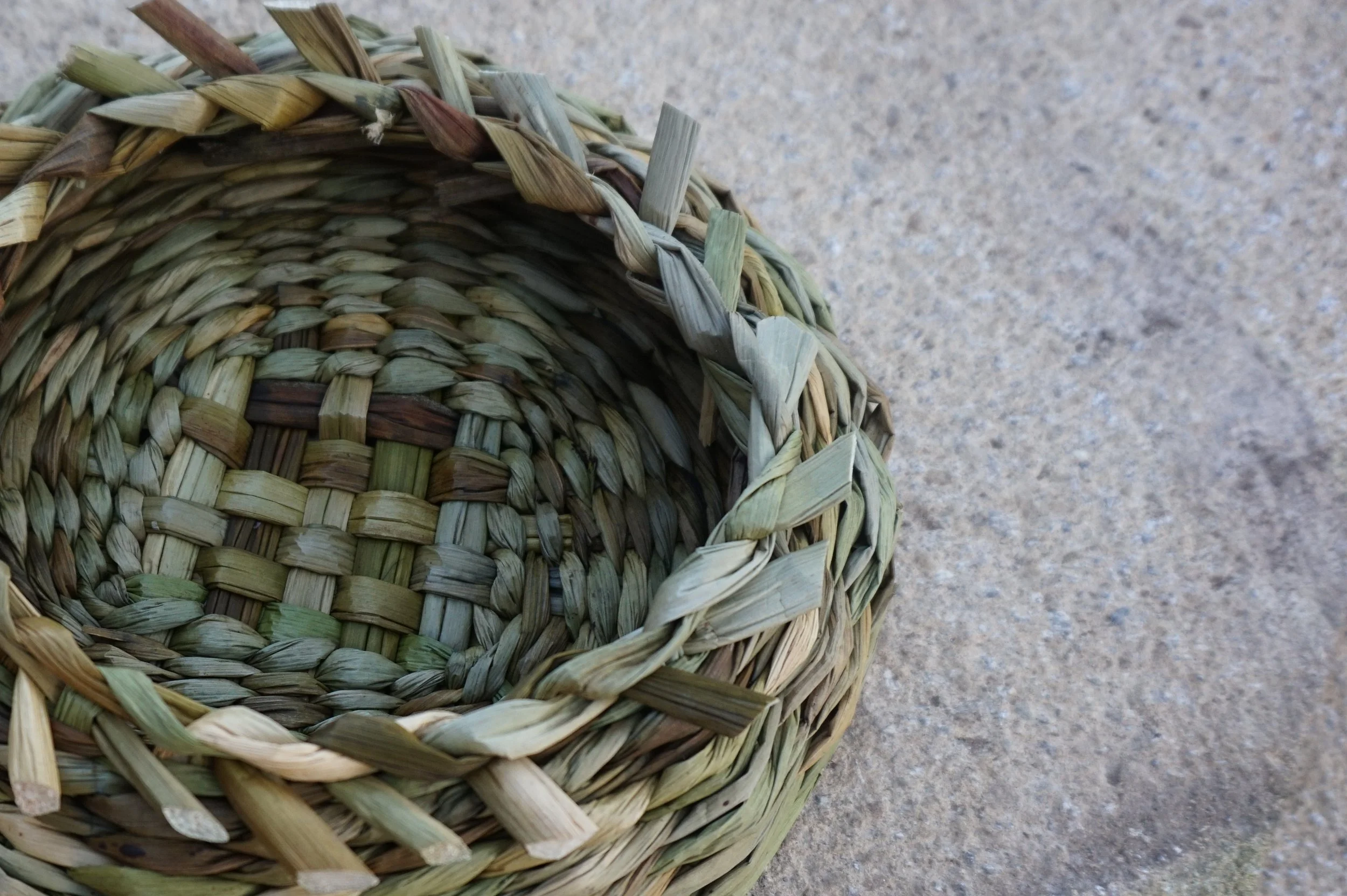 Close-up of a woven straw basket placed on a concrete surface, showing detailed weaving patterns of dried grass or straw.