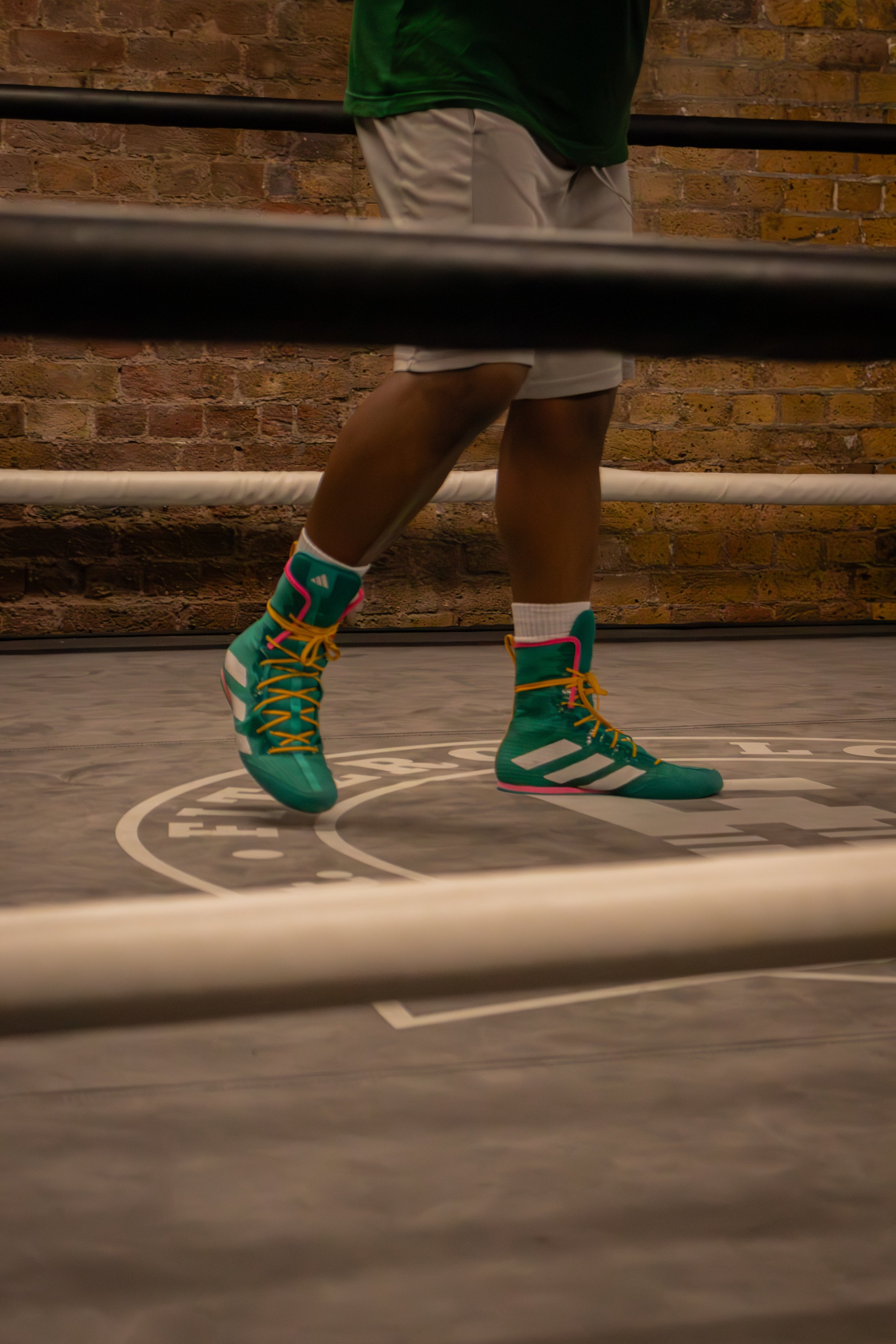 A person in colorful basketball shoes practicing in a gym with brick walls and padded floors, viewed through a basketball hoop.