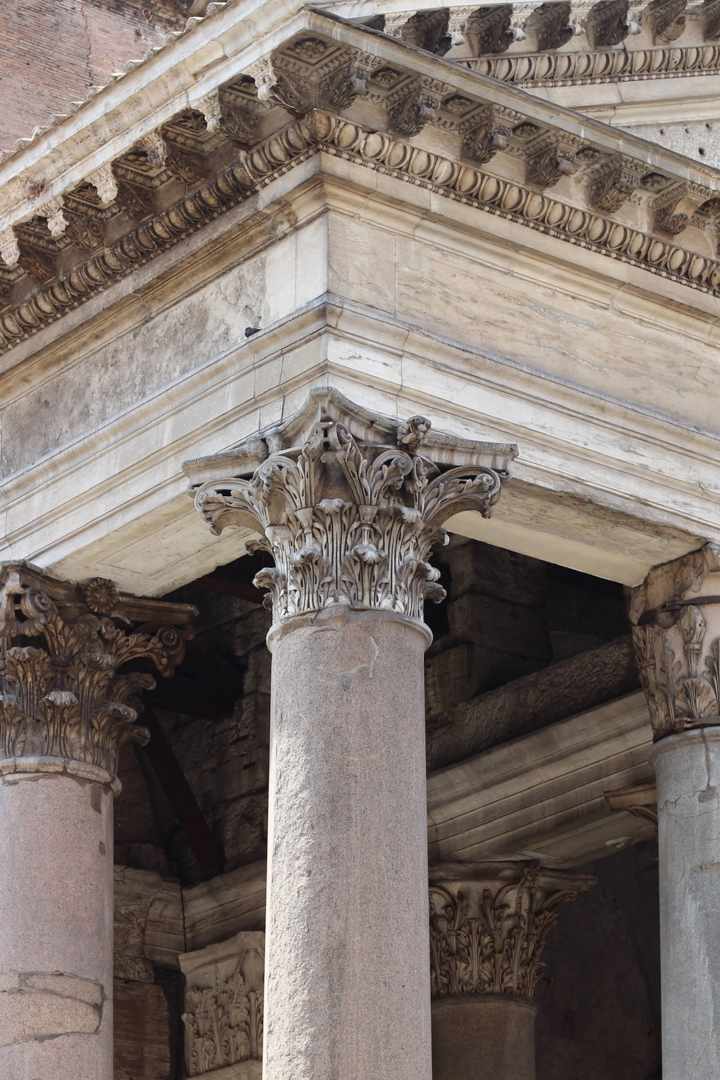 Close-up of ancient stone columns with Corinthian capitals supporting an elaborately carved stone entablature in a historic structure.