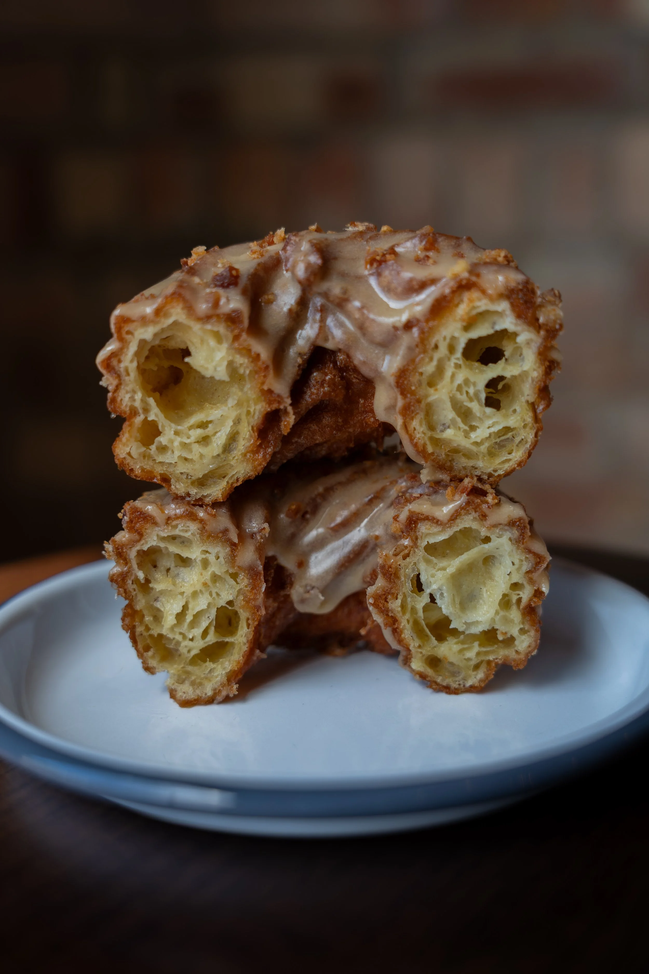A close-up of a cruller,  a deep-fried pastry with a golden-brown crust, topped with white icing, served on a white plate.