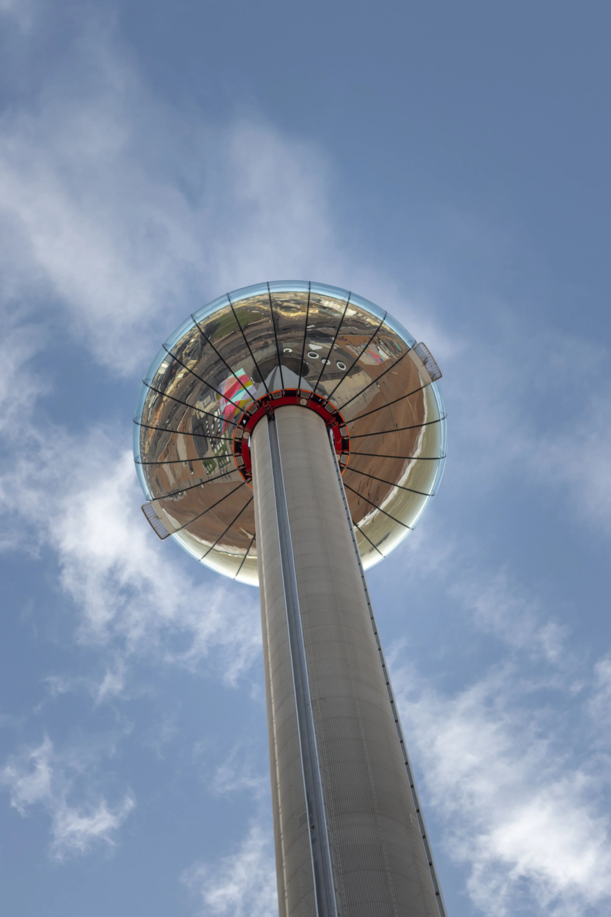 A tall observation tower with a reflective, spherical top against a partly cloudy blue sky in Brighton, United Kingdom.
