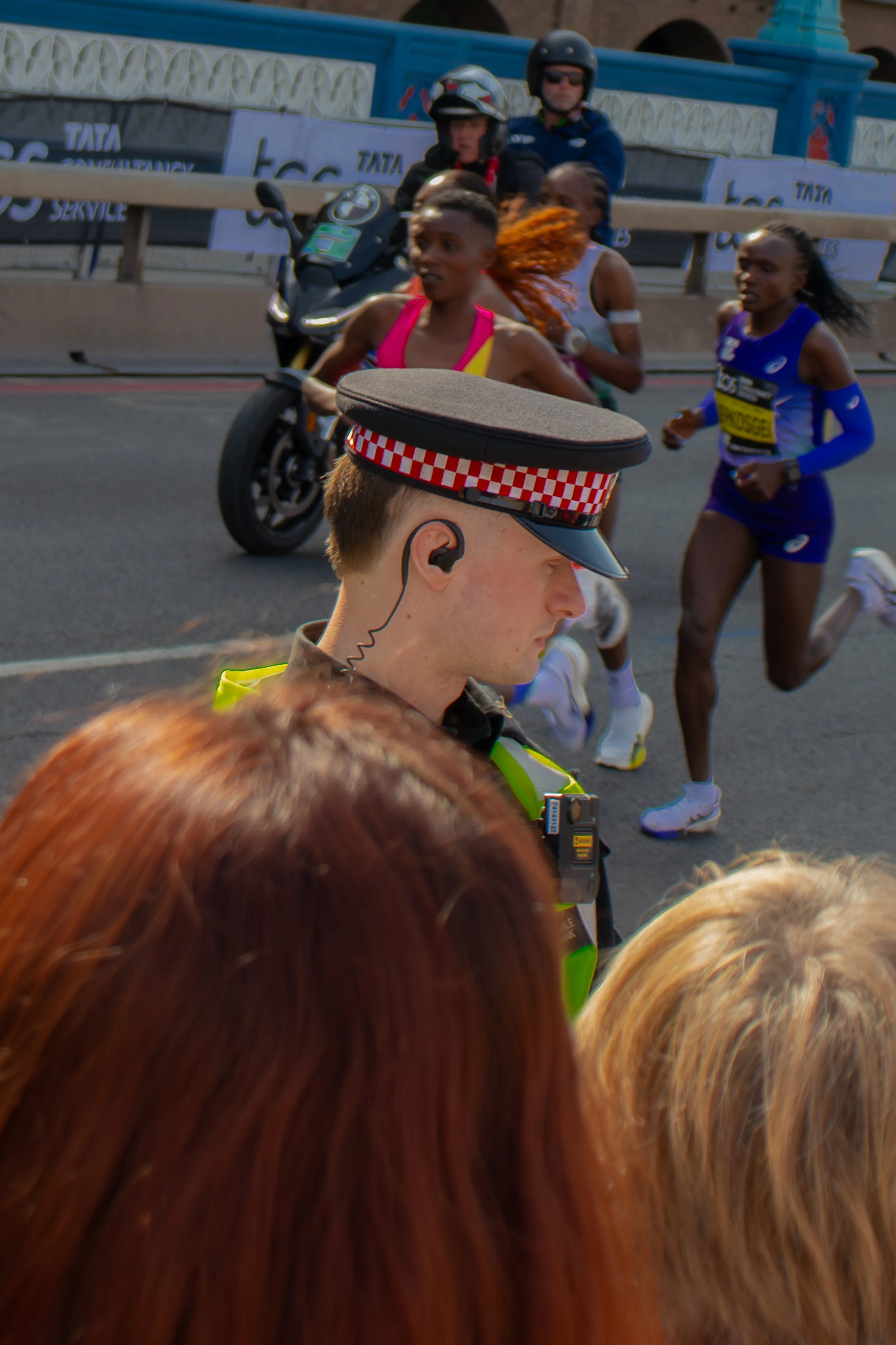 A group of elite runners participating in the London Marathon with runners of various ages and ethnicities. Some are wearing sports gear and race bibs.