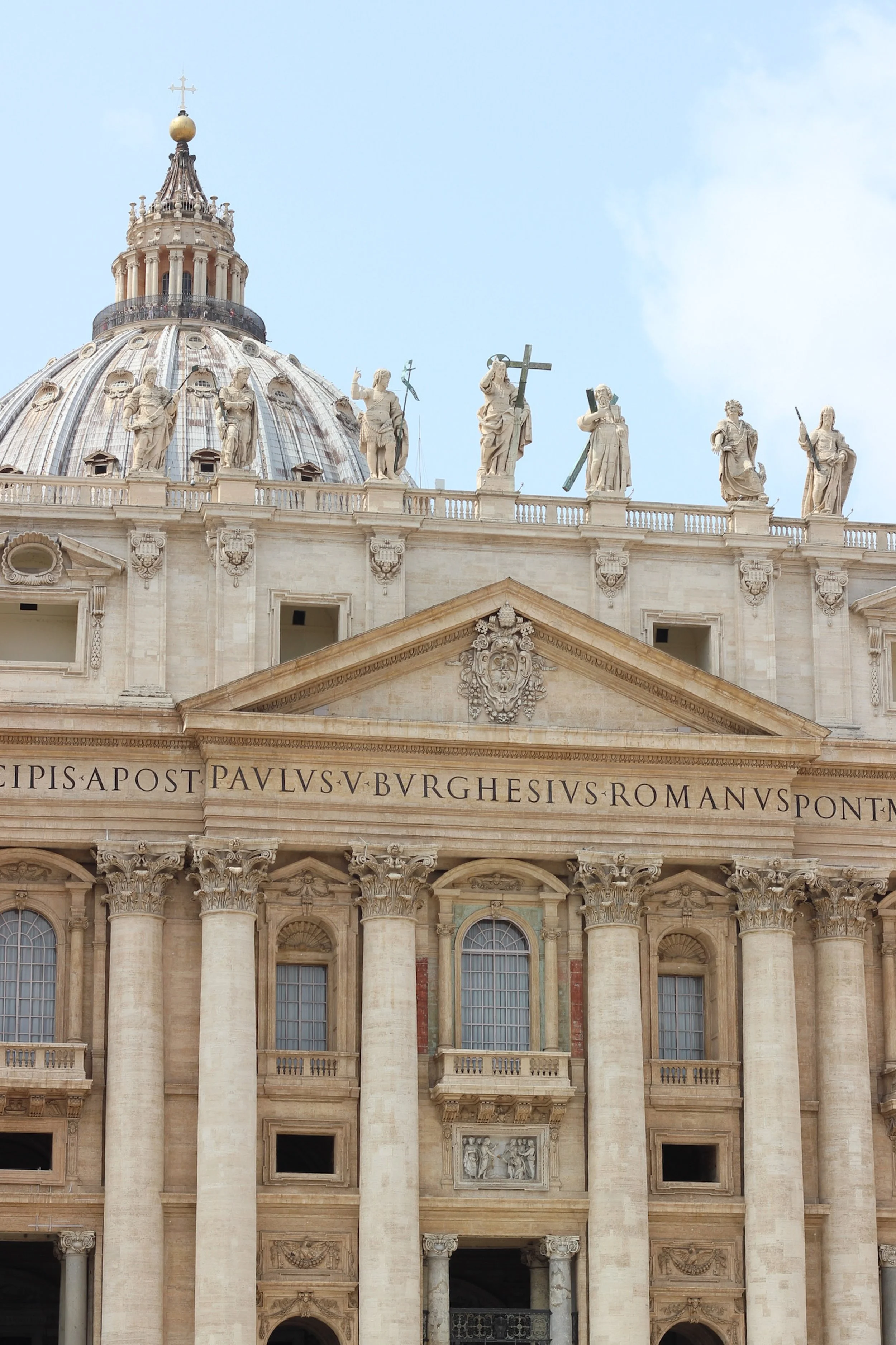 Facade of St. Peter's Basilica in Vatican City with statues of saints on top and columns in the front.