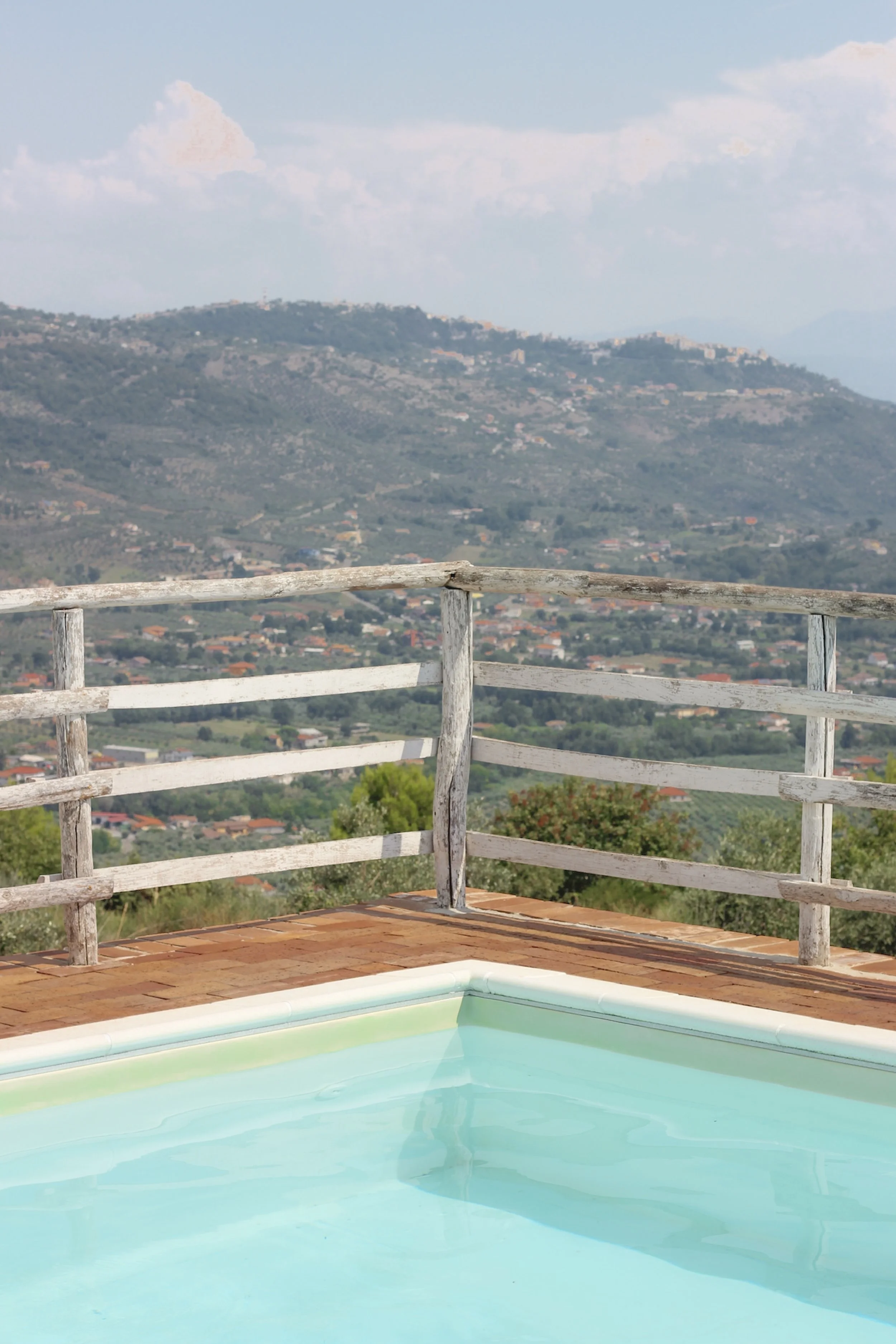 View of a swimming pool with a wooden fence and a scenic mountainous landscape in the background in Italy.