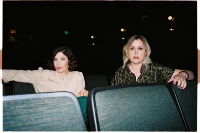 Carrie Brownstein and Corin Tucker of Sleater-Kinney sitting in an auditorium with empty seats in front of them