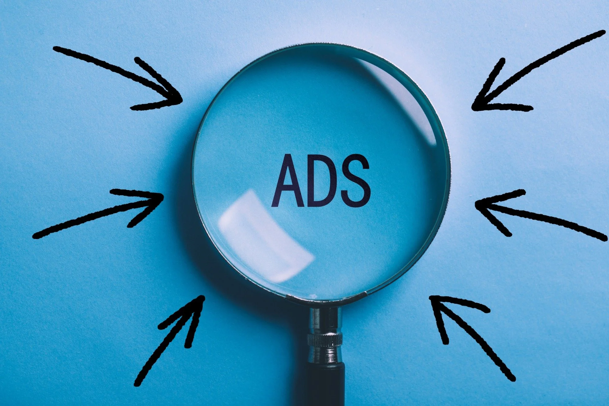 A magnifying glass with the word 'ADS' inside, surrounded by black arrows pointing towards it against a blue background.