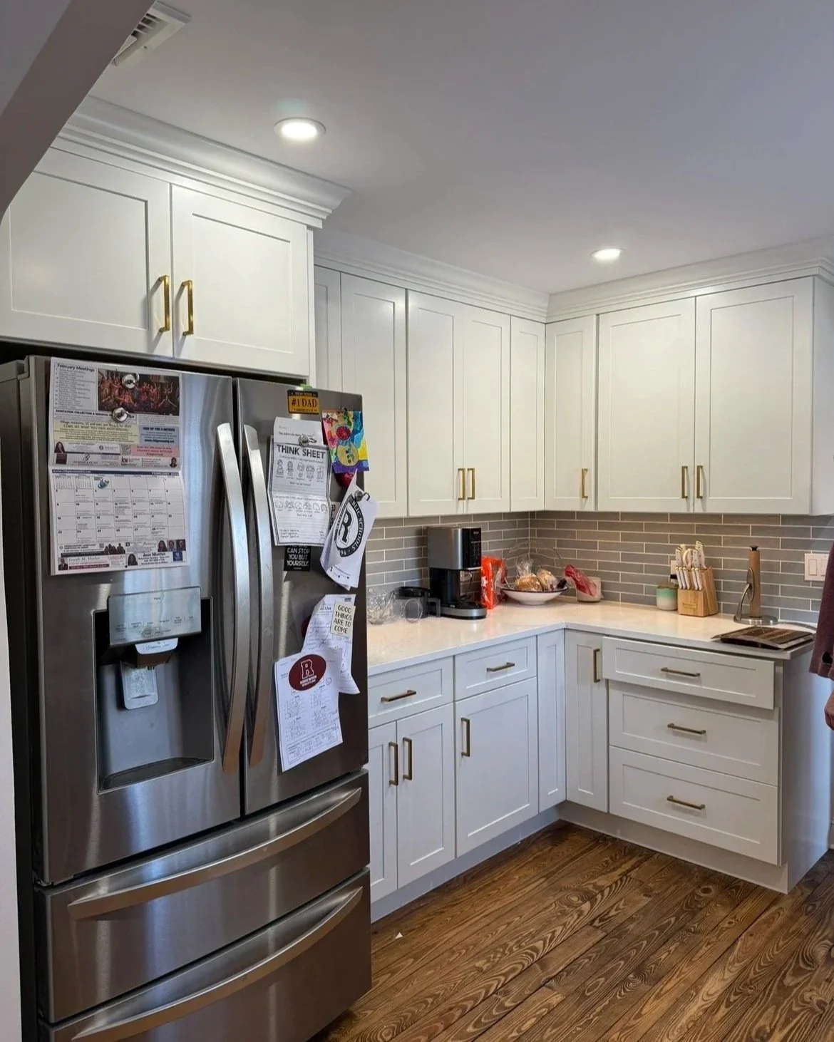 Kitchen with white cabinets, a stainless steel refrigerator, wooden flooring, and small appliances on the counter.