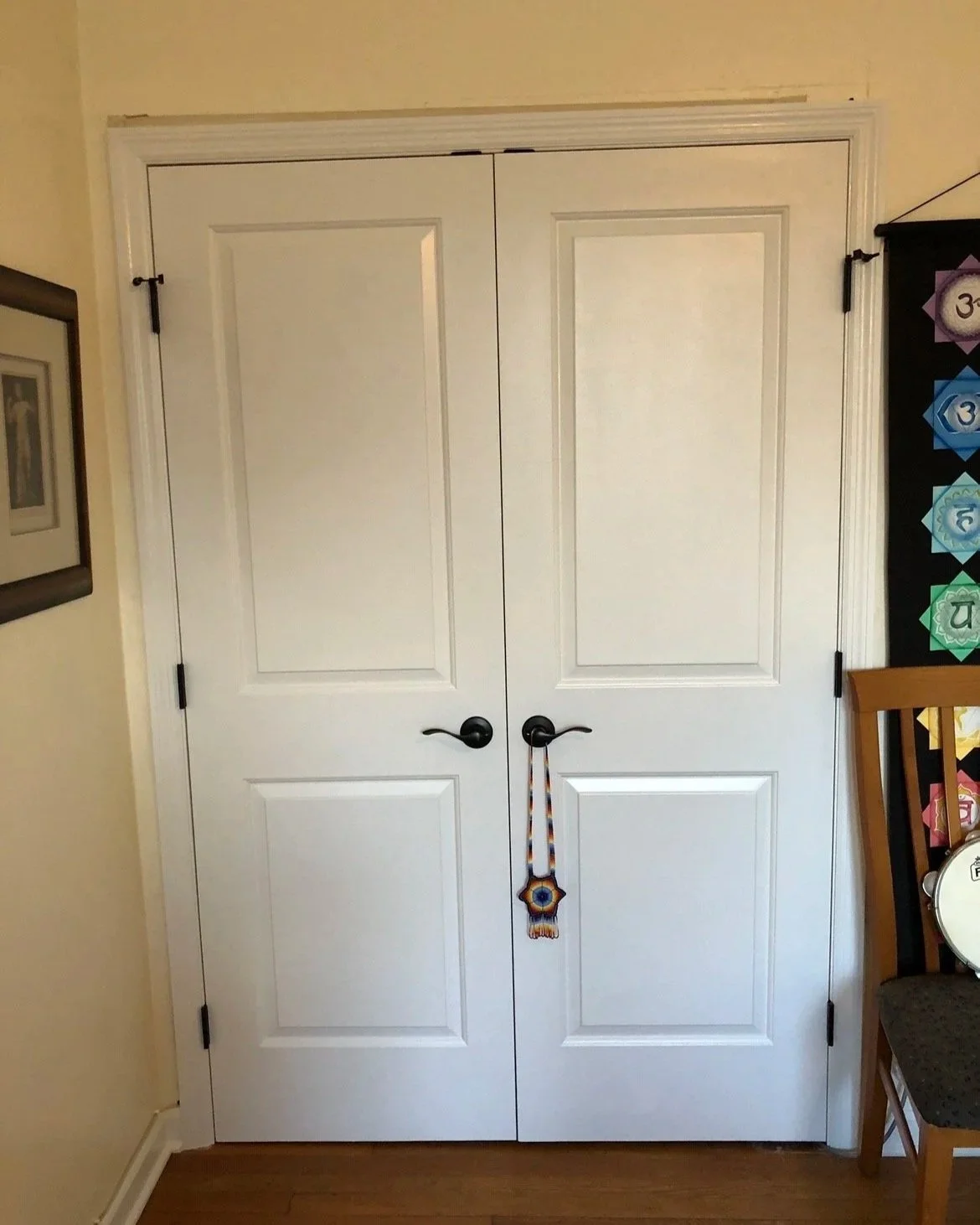 White double closet doors with black handles, decorated with a beaded hanging ornament.