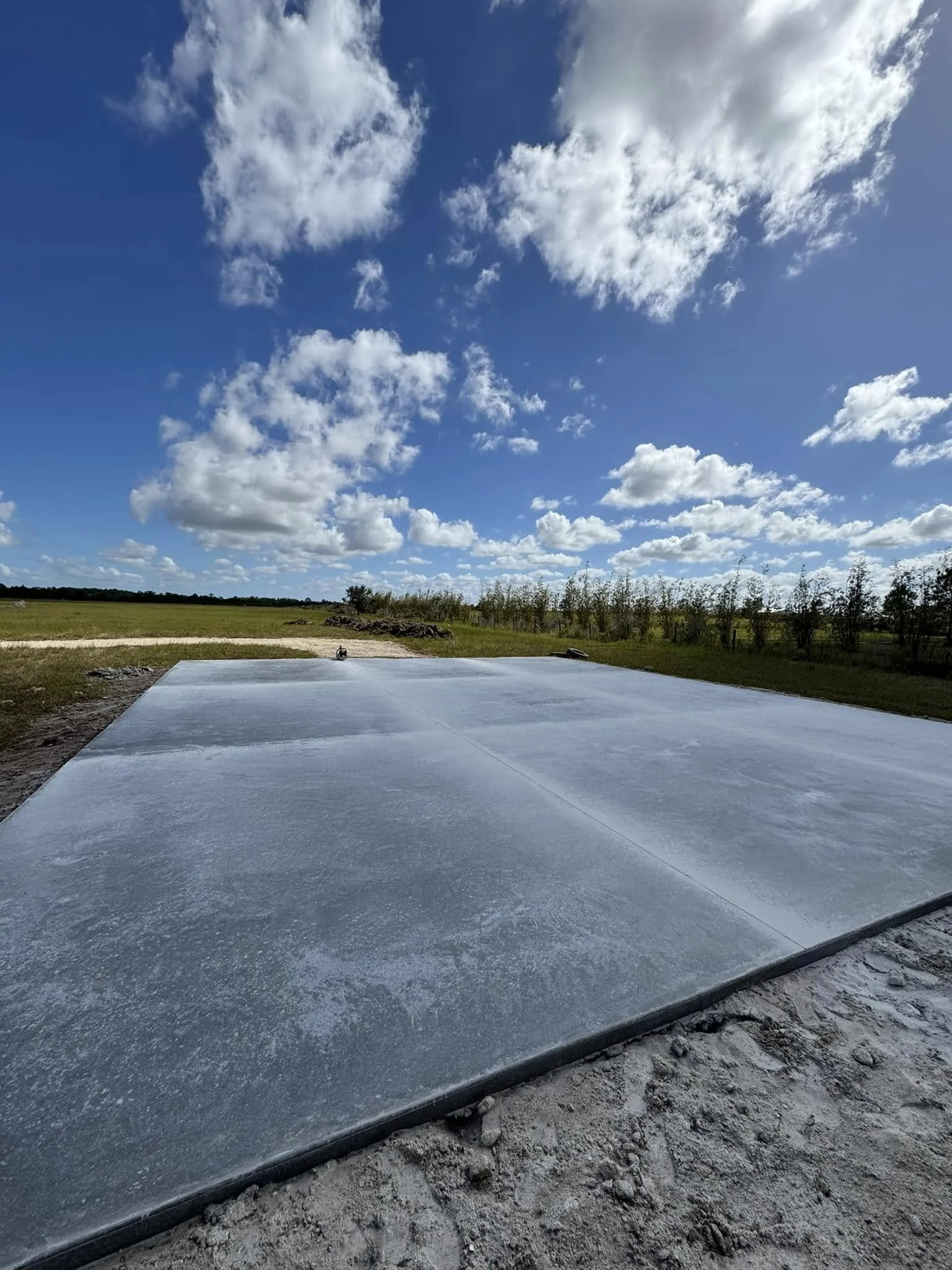 Concrete slab on a construction site with a grassy field and partly cloudy blue sky in the background.