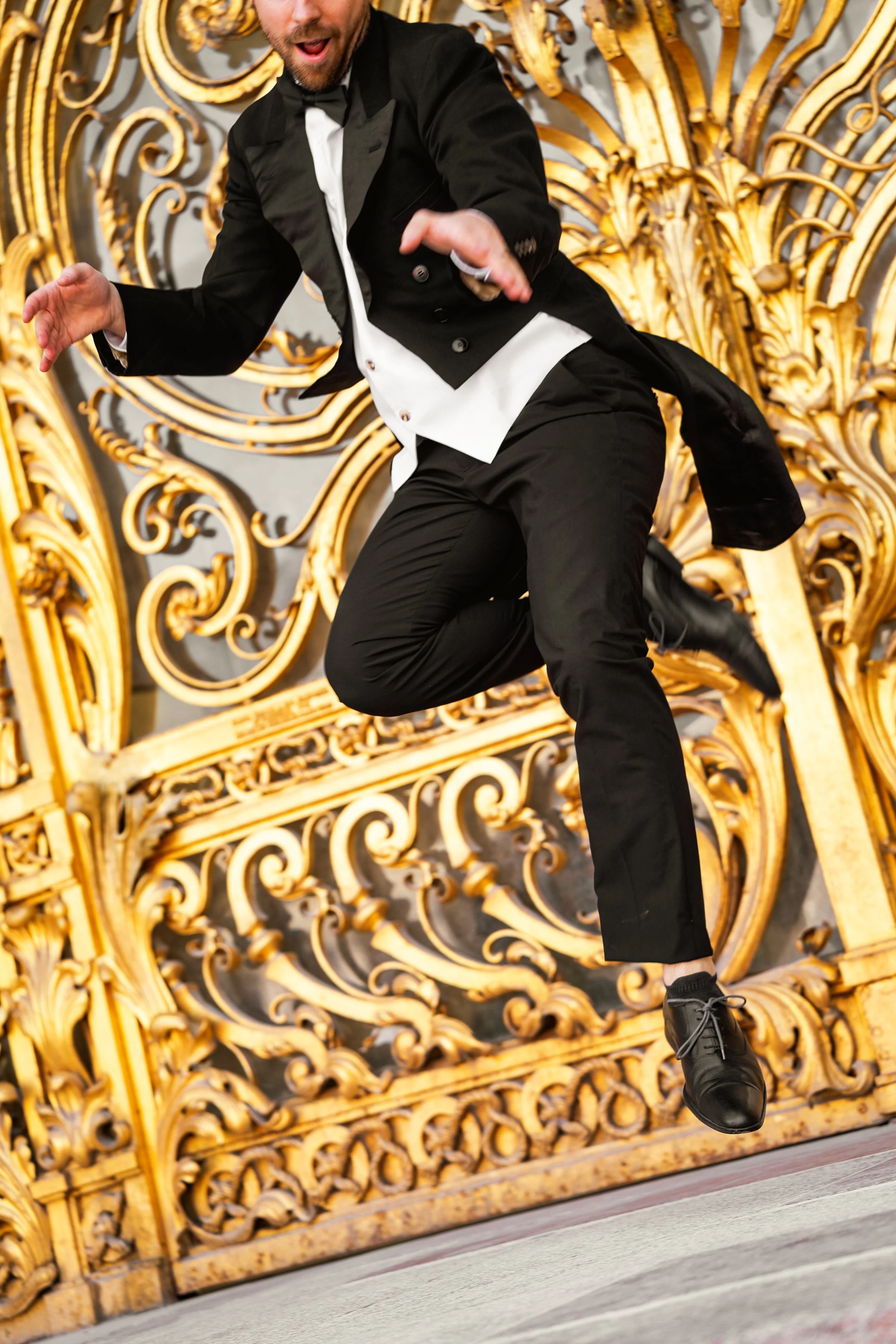 Danseur Gatsby en costume noir queue de pie dansant devant une grille dorée ornée