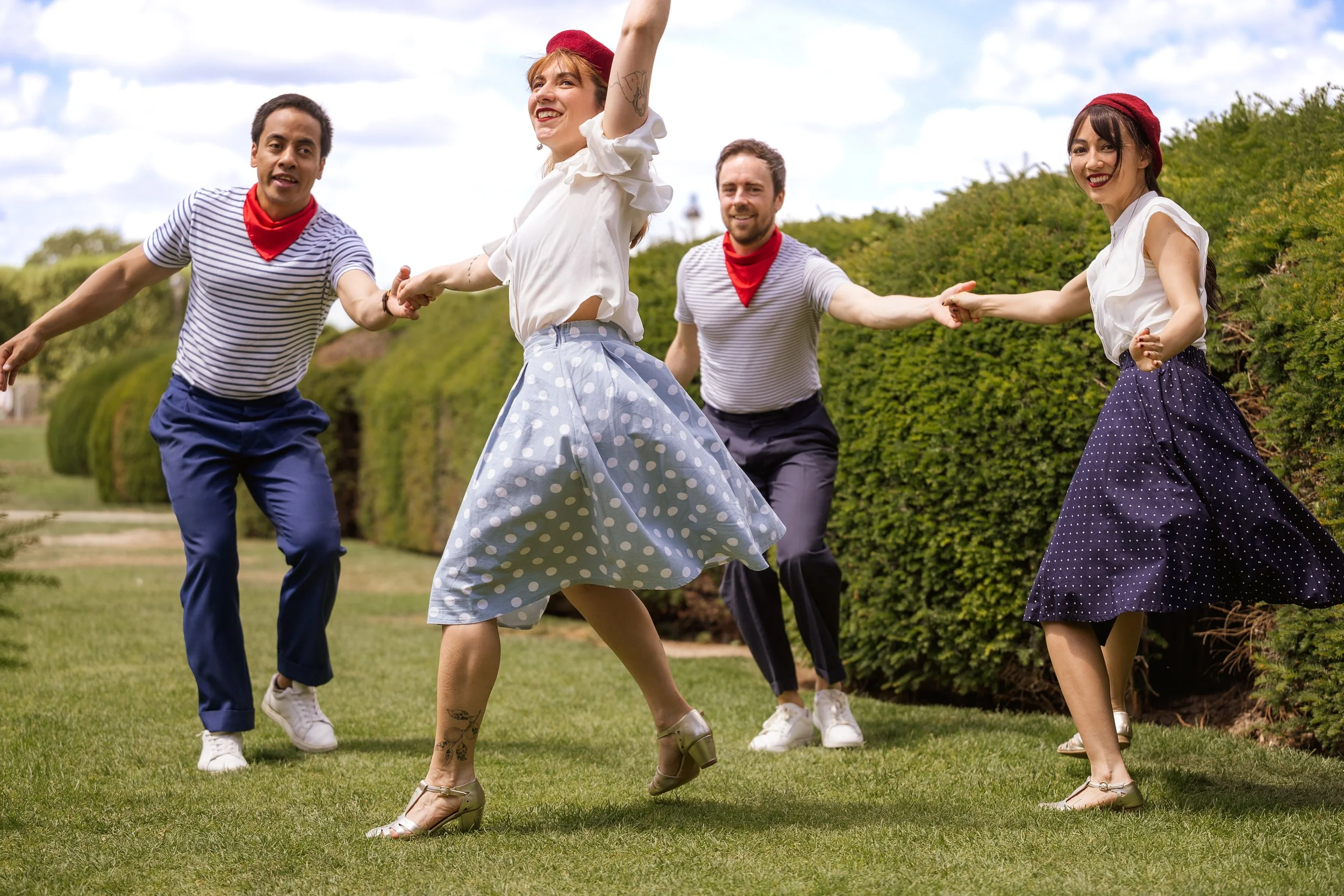 Quatres danseurs swing en tenue de guinguette française dansant dans un parc avec joie