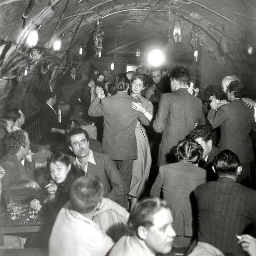 Gens dansant dans une salle avec un plafond en arc, ambiance rétro, en noir et blanc.