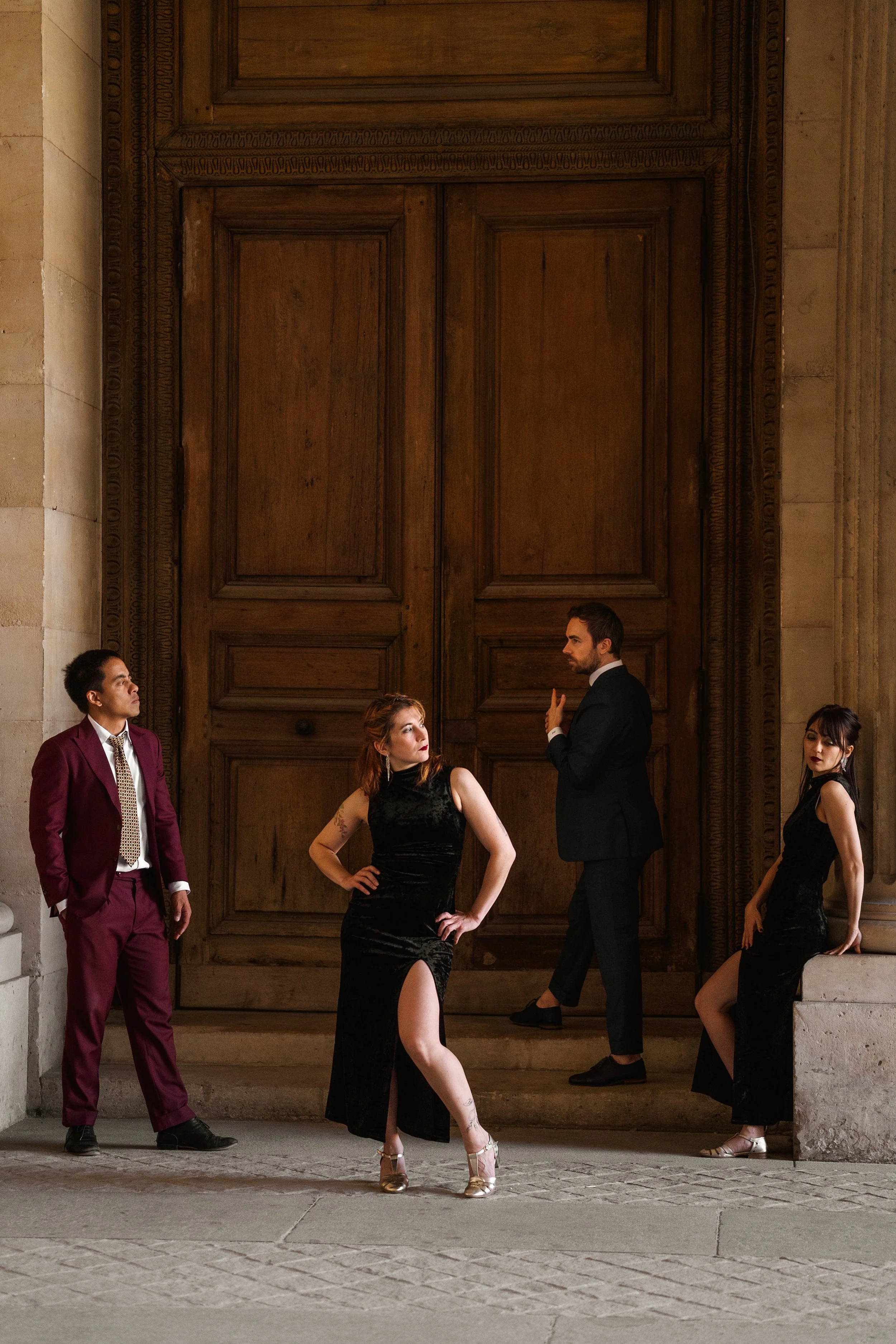 Un groupe de quatre danseurs swing habillées élégamment, posant devant une grande porte en bois dans un bâtiment en pierre.