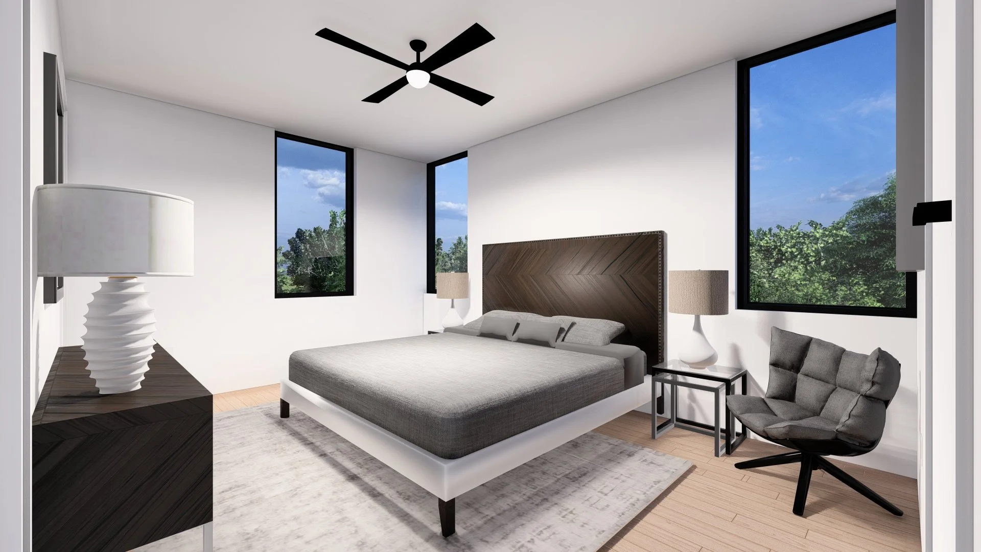 Modern bedroom with a large bed, two white nightstands with lamps, a gray lounge chair, two large windows with trees outside, a black ceiling fan, and a light-colored rug.