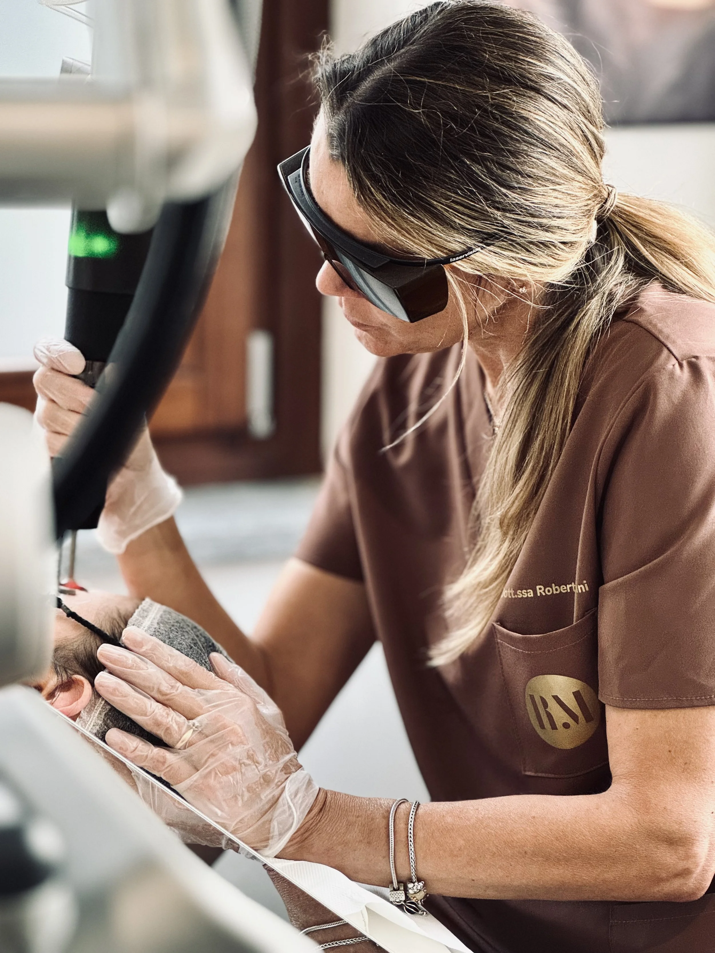 Una dottoressa in abbigliamento medico utilizza un microscopio per un'esame su un paziente disteso in posizione supina.