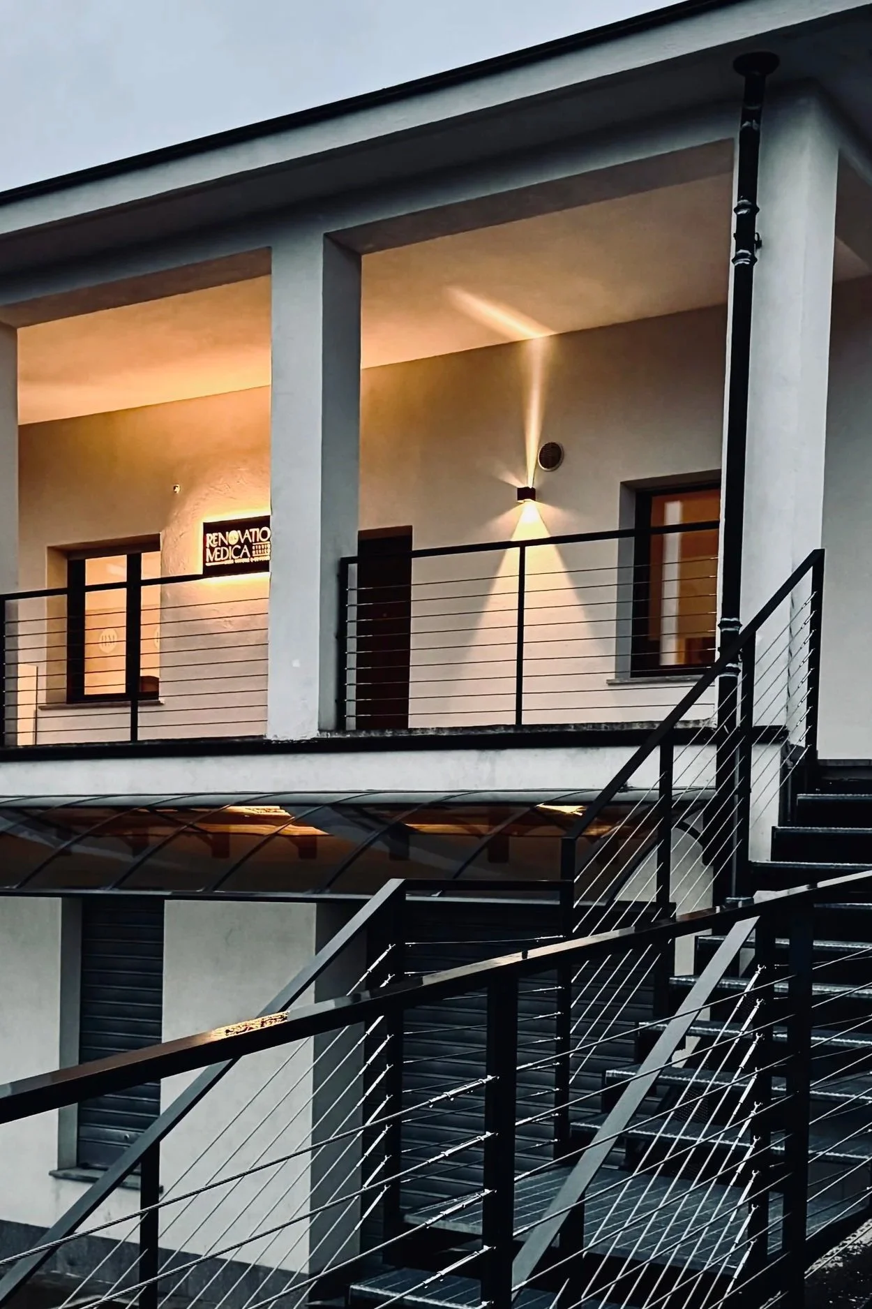 Edificio con balcone illuminato, pareti di colore chiaro, finestra con inferriata e insegna luminosa che dice 'Rinnovato Medica'.