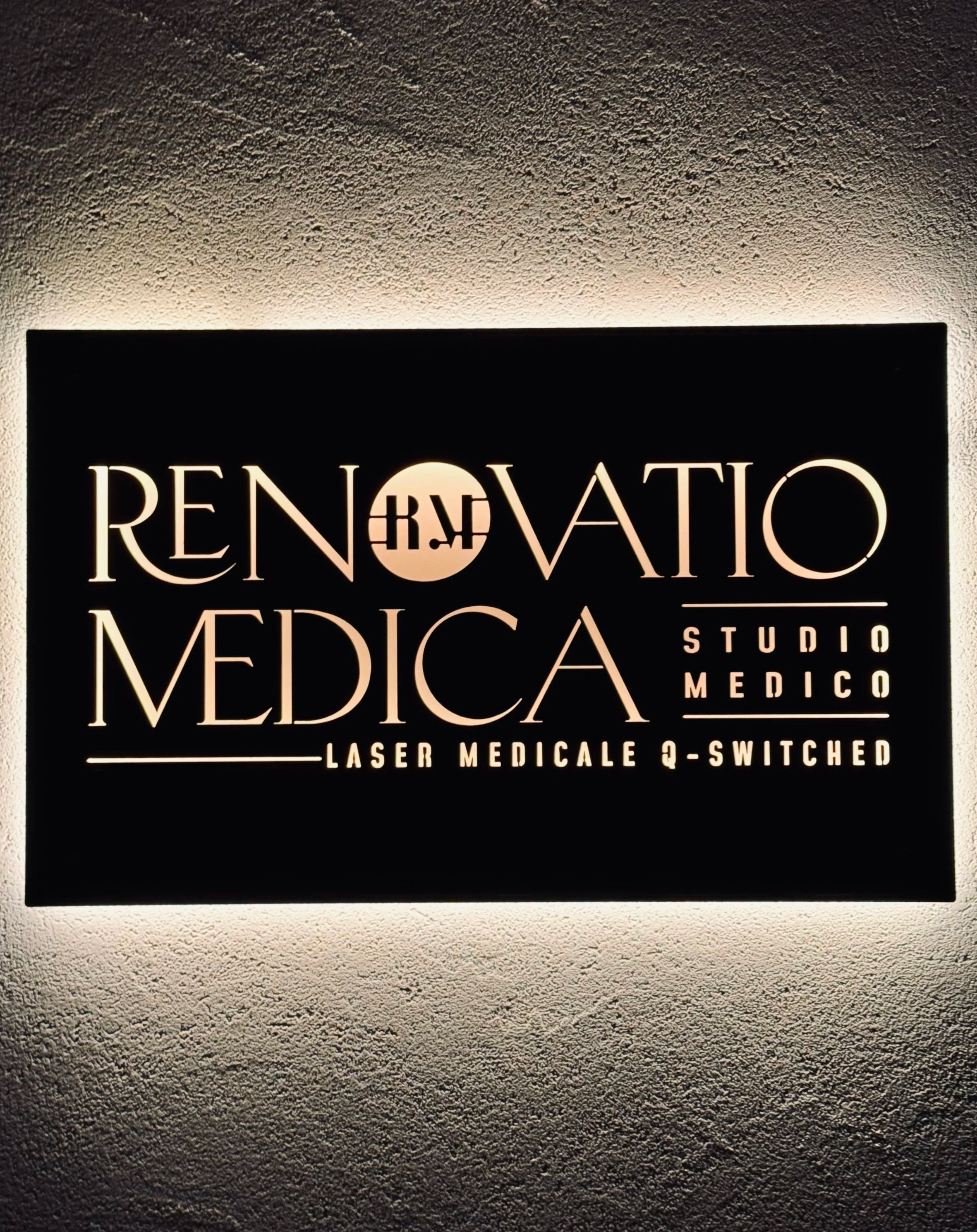 Pannello luminoso con testo 'RINOVATIO MEDICA', 'STUDIO MEDICO', e 'LASER MEDICALE Q-SWITCHED' su parete bianca.
