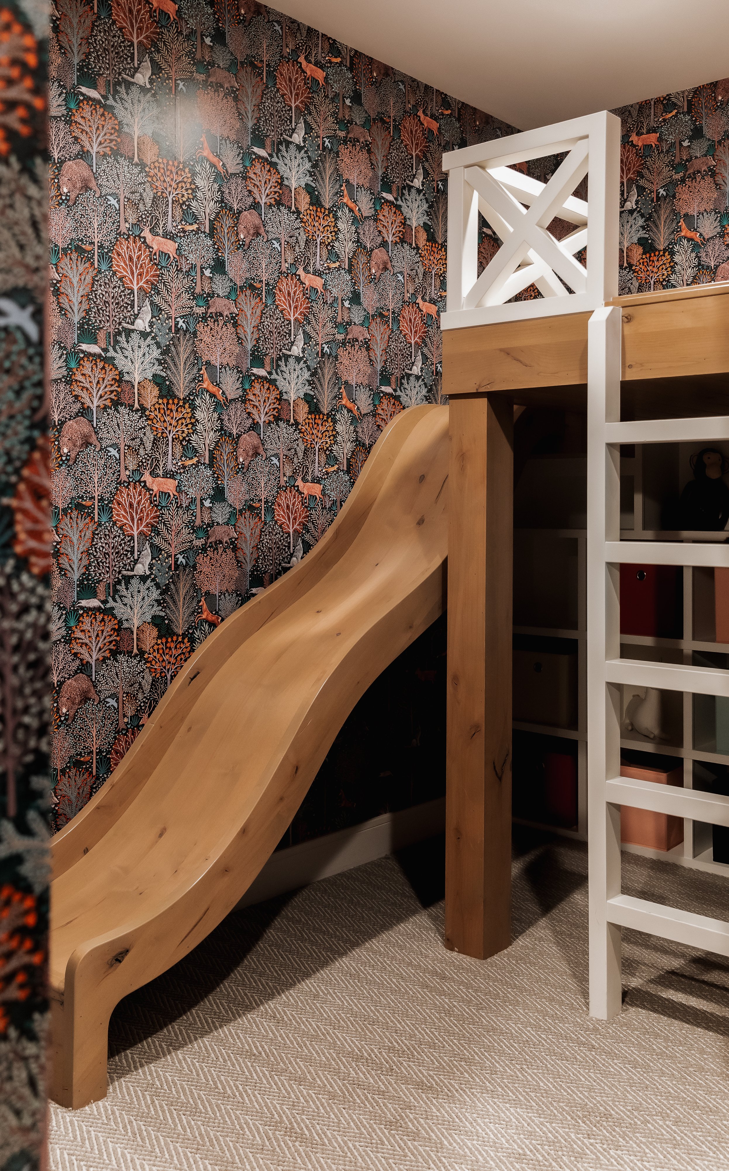 A wooden indoor slide next to a colorful forest-themed wallpaper with animals and trees.