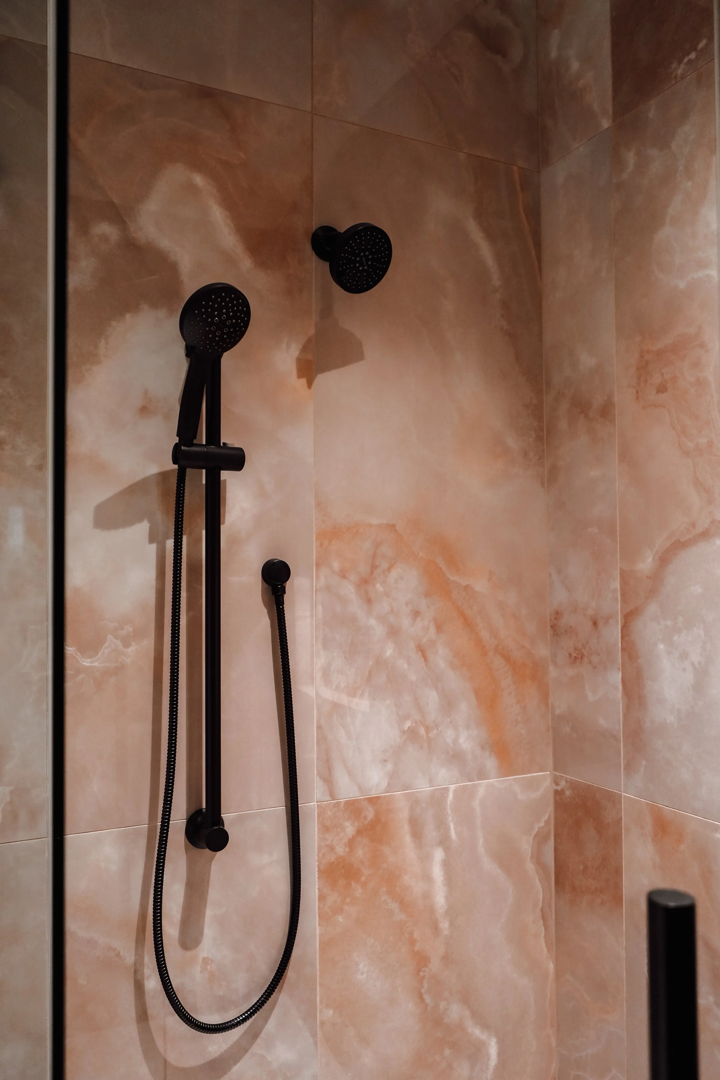 Black showerhead with attached handheld shower wand mounted on a tiled bathroom wall.