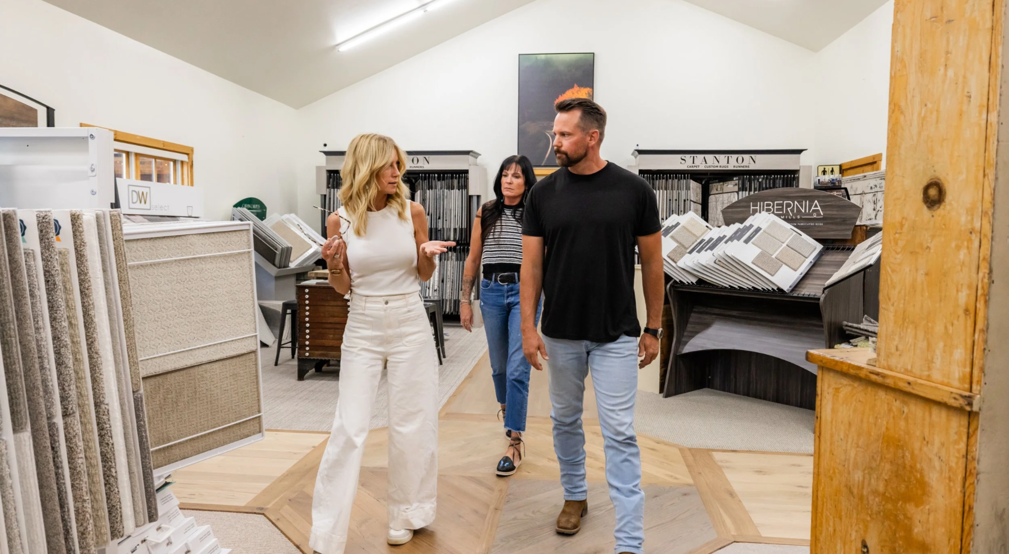 Three people shopping inside a flooring store, with samples of carpets and rugs displayed around them.