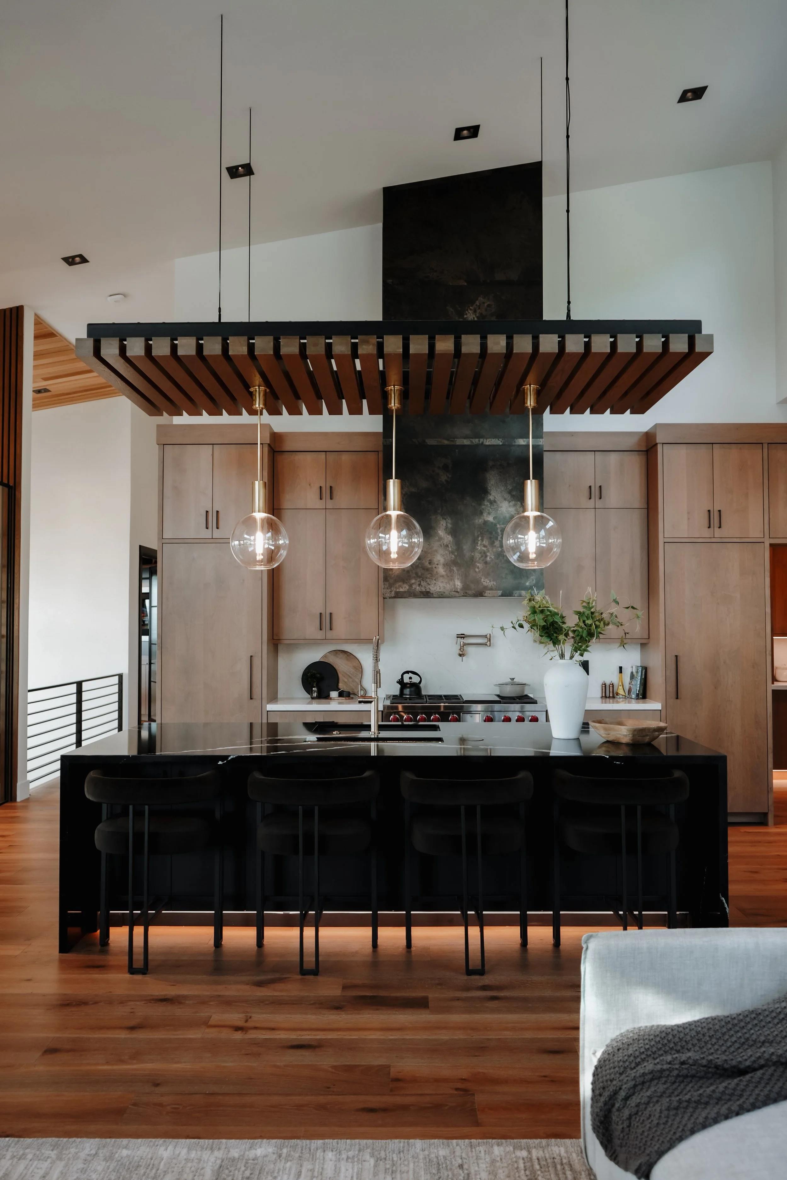 Modern kitchen with black island, wooden cabinets, and three pendant lights.