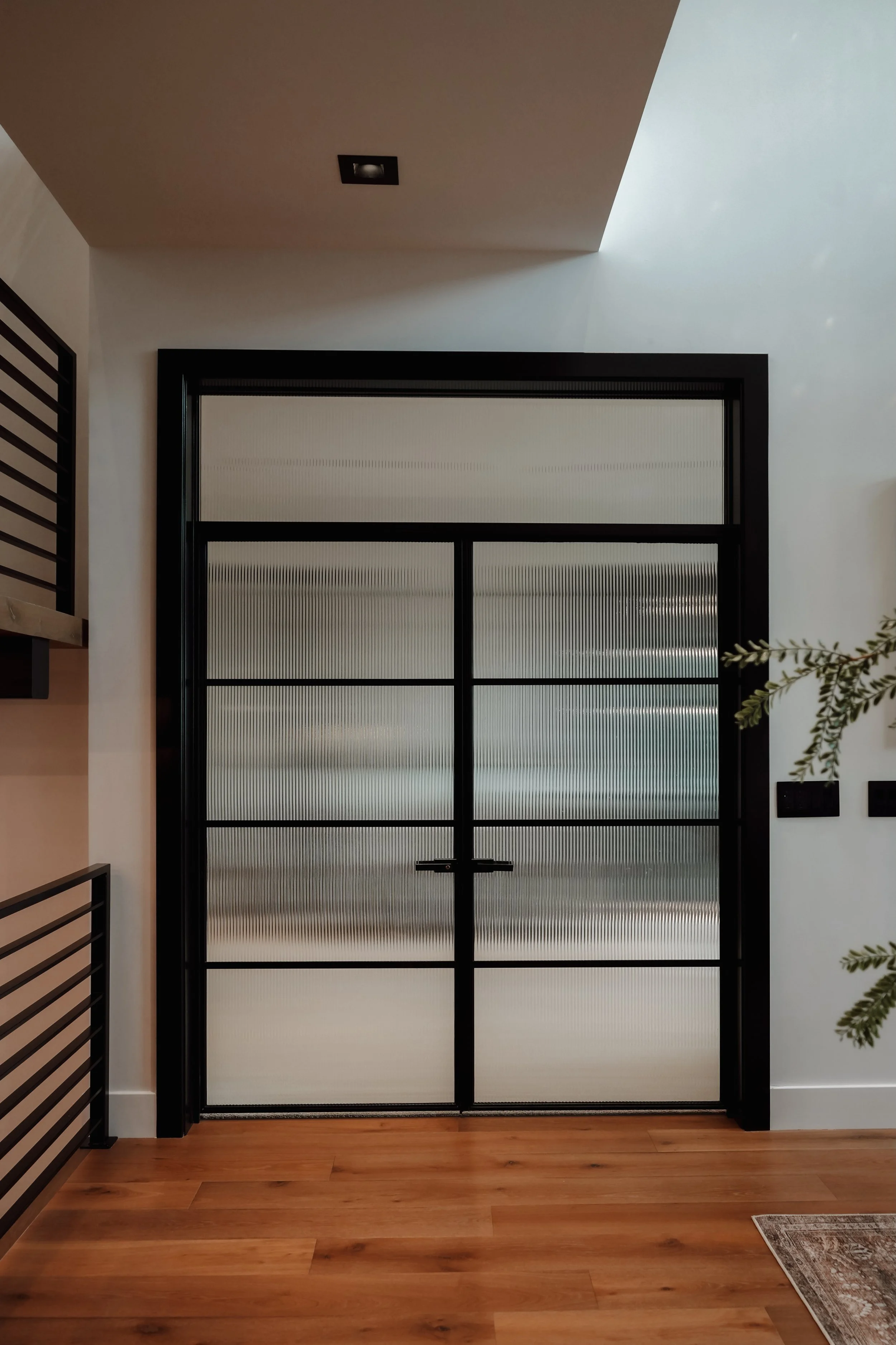 Modern black-framed glass door with frosted glass panels in a room with wooden flooring and white walls.