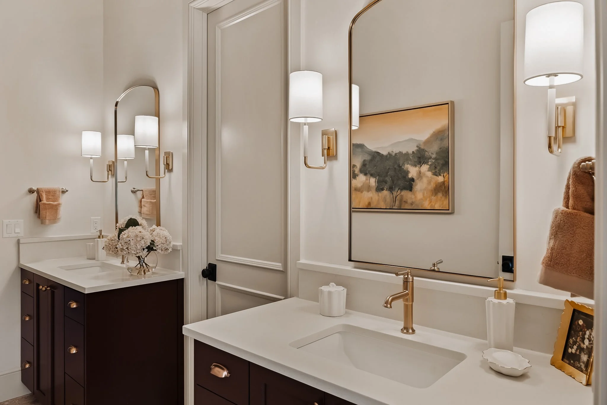 Beautiful modern bathroom with dual vanities, large mirror, gold fixtures, wall-mounted lights, and decorative towels.