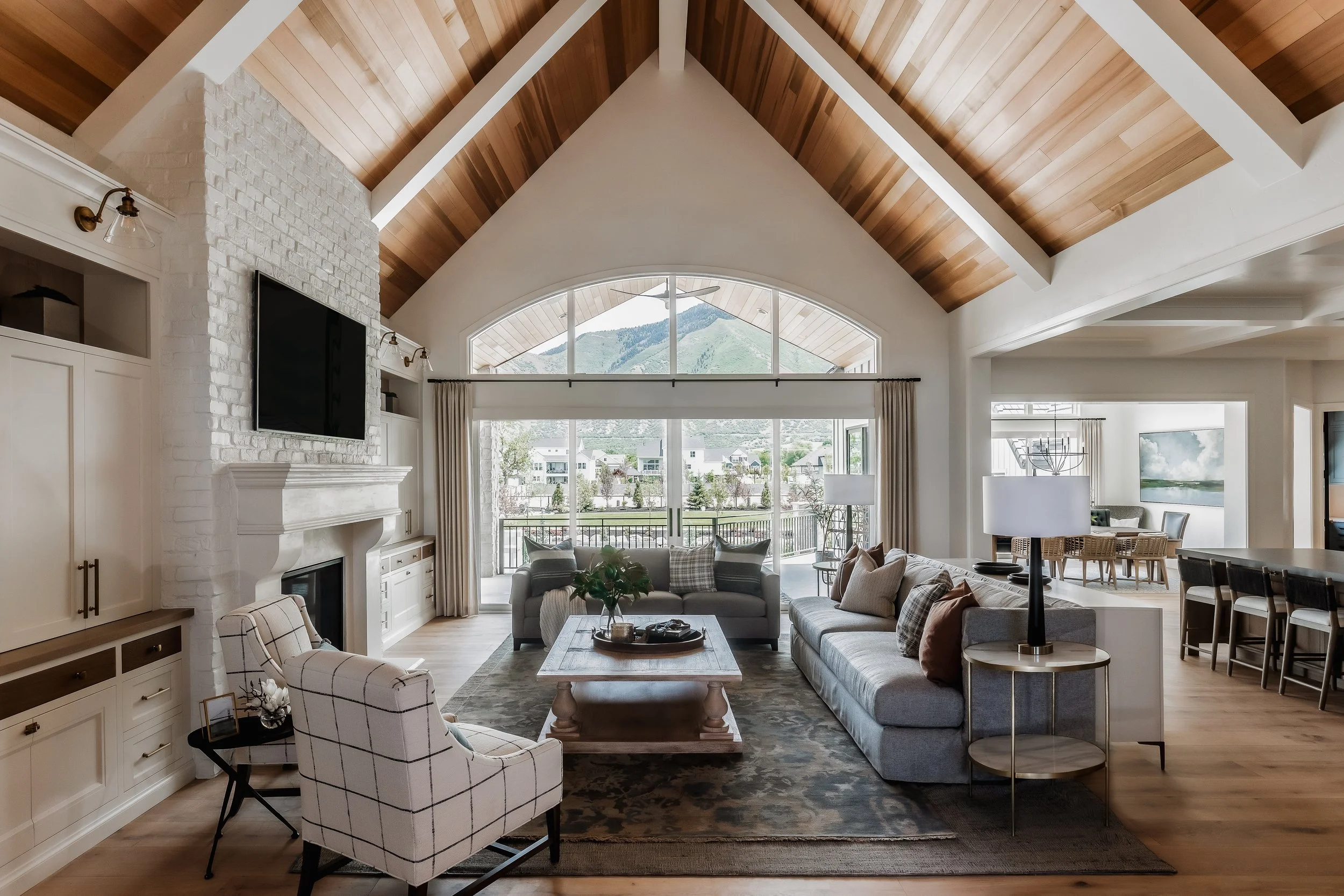 Living room with vaulted ceiling, white brick fireplace, large windows overlooking mountains, and various seating including sofas and armchairs.