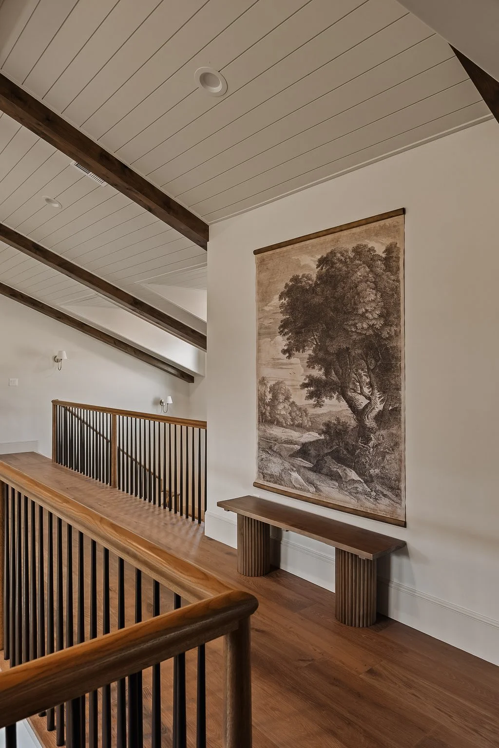 Interior view of a room with a long wooden railing, a decorative tapestry of a tree on the wall, and wooden beams on the ceiling.