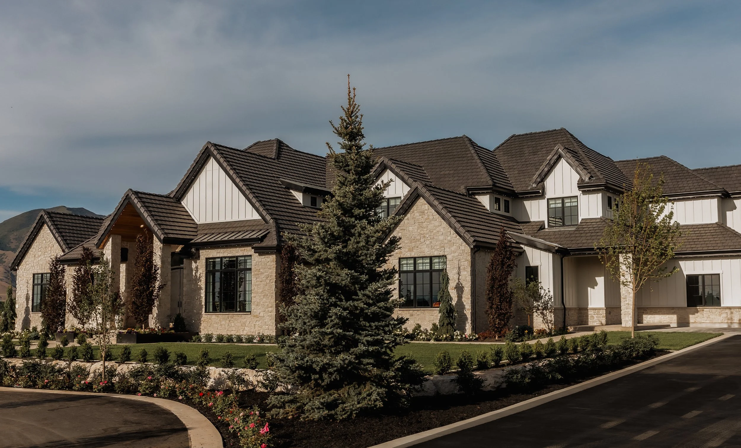 A large modern house with stone and white siding, multiple gabled roofs, and surrounded by landscaped yard and trees.