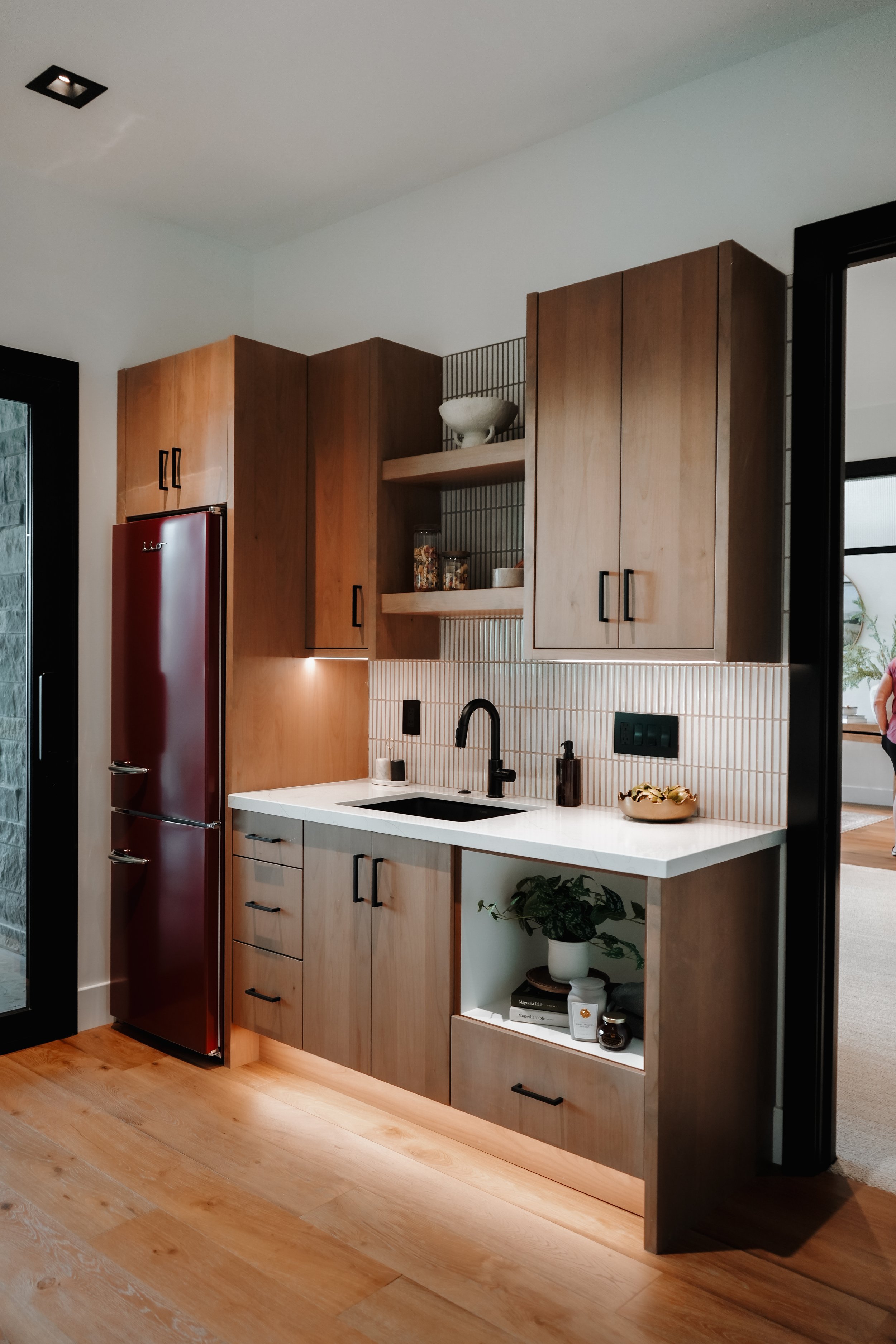 Modern kitchen with wooden cabinets, white countertop, black faucet, small indoor plant, and a red refrigerator.