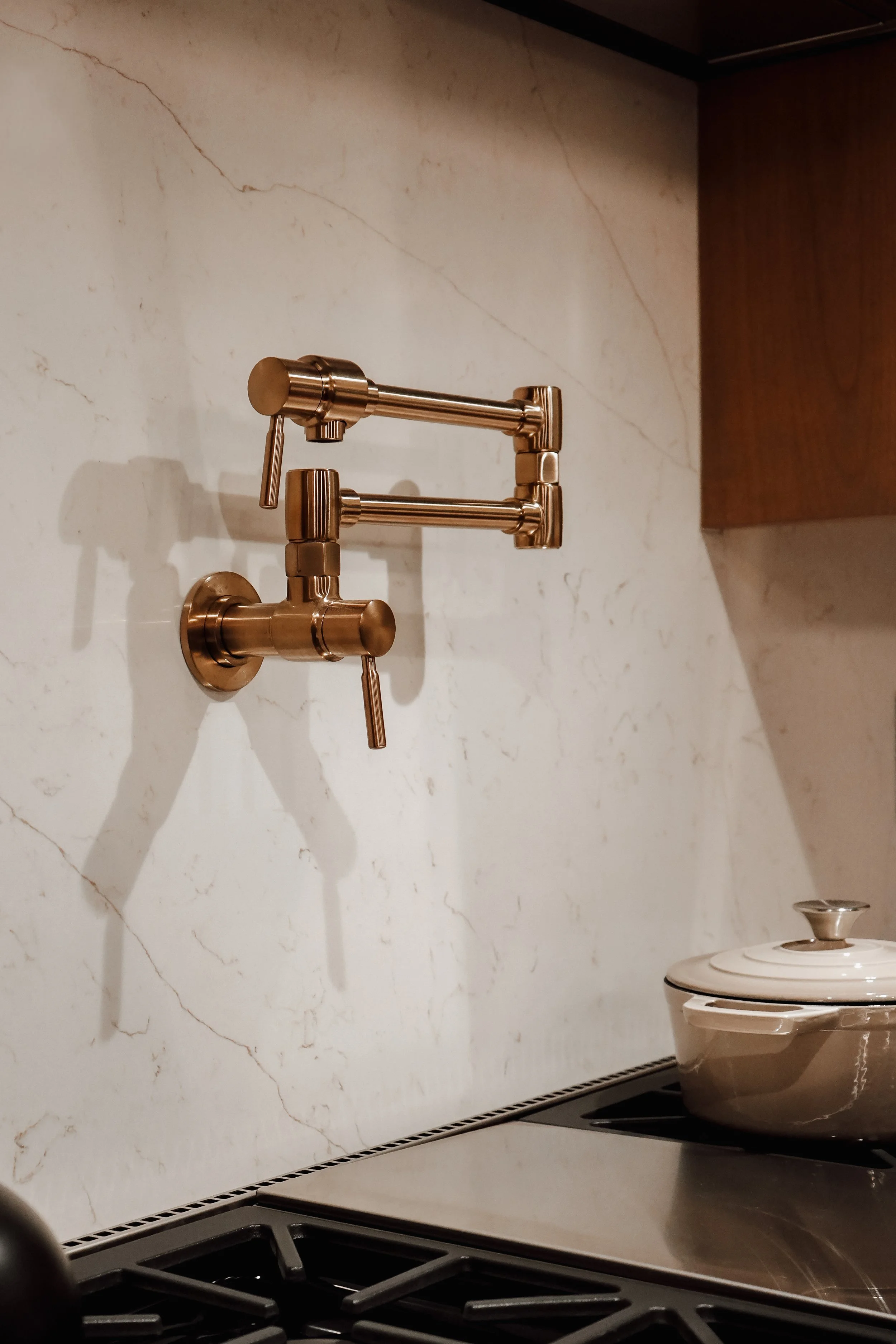 Kitchen with brass pot filler faucet, stovetop, and a pot with a lid on the counter.