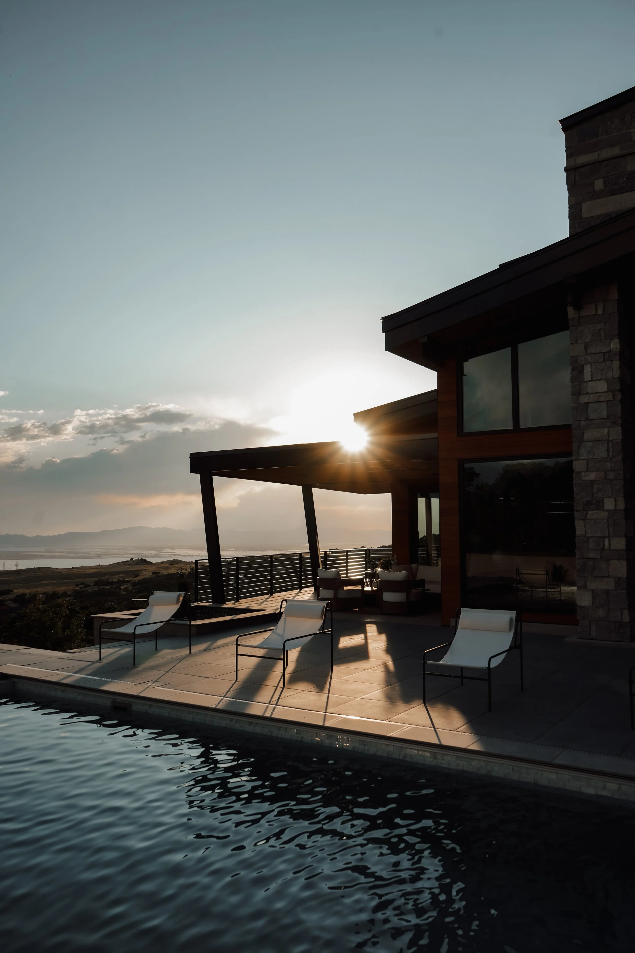 Modern house with outdoor patio and pool, sunset in the background, scenic landscape with mountains and water