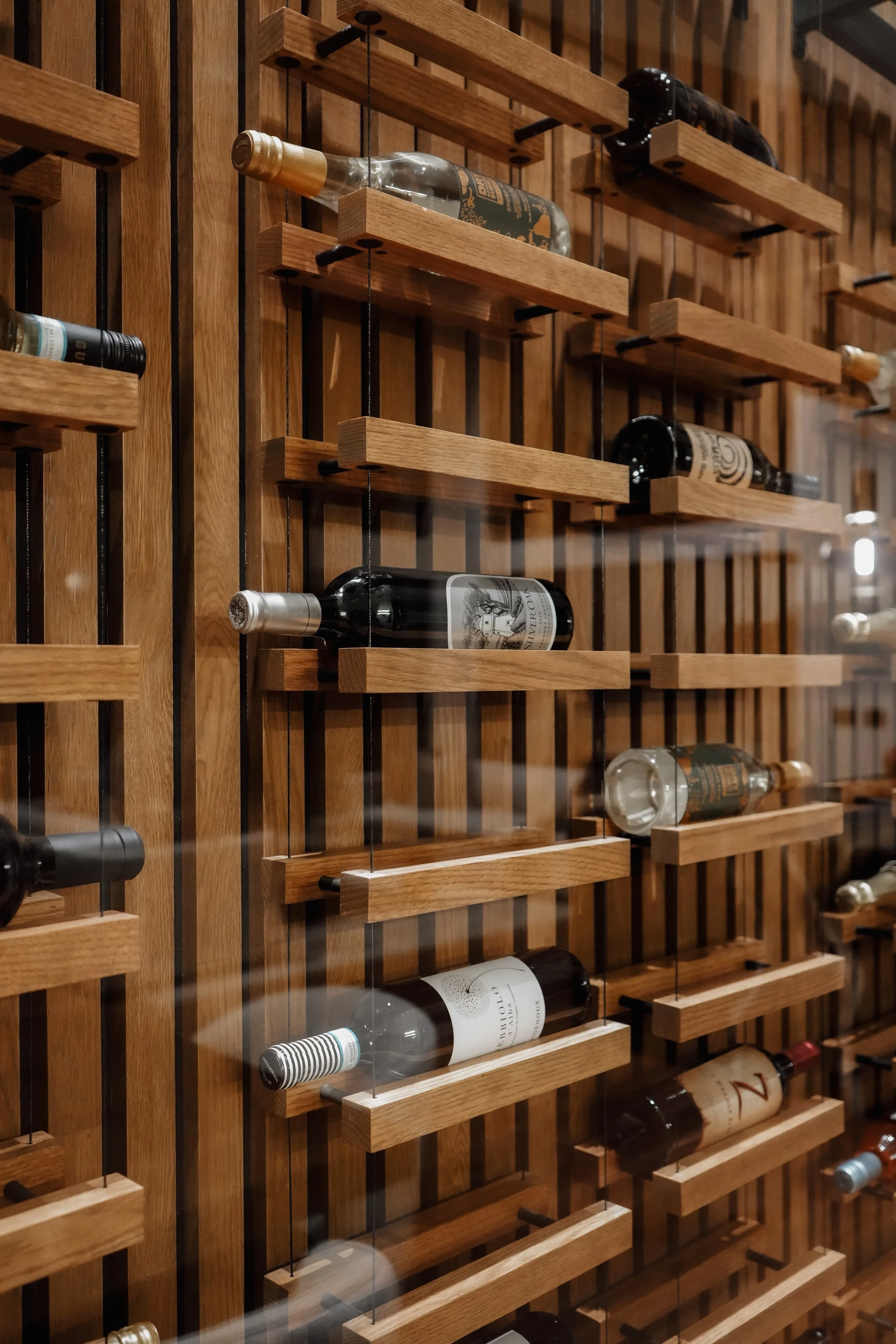 Wine bottles displayed horizontally on wooden racks behind a glass panel.