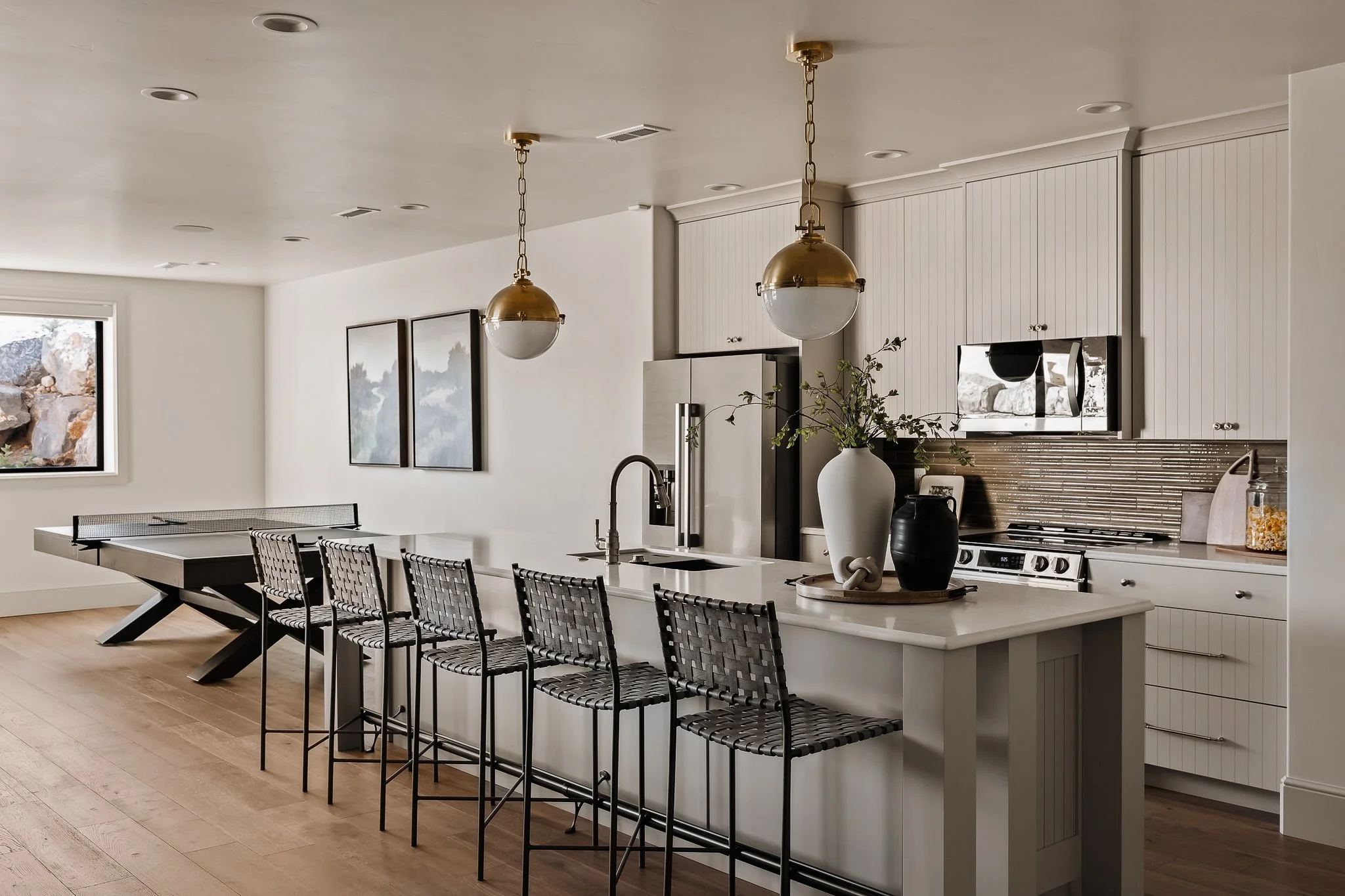 Modern kitchen with white cabinetry, a marble island with bar stools, pendant lights, and a stainless steel refrigerator and oven.