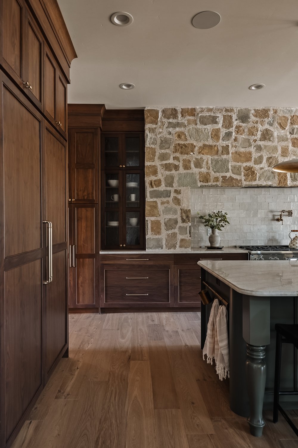 A kitchen with wooden cabinets, a stone accent wall, a white countertop, and a potted plant.