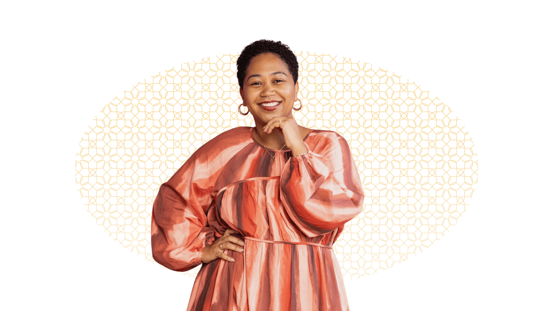 Anela Malik shown with short curly hair, wearing a colorful, patterned, long-sleeved dress, smiling, with her hand on her chin, in front of a background with a golden, geometric pattern.