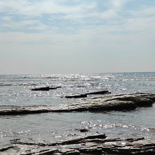 Ocean with waves and rocks under a partly cloudy sky.