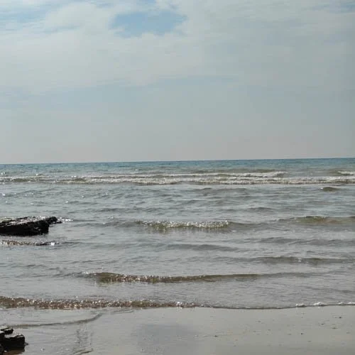 Calm ocean waves at a sandy beach under a cloudy sky.