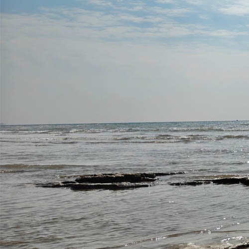Calm beach with waves and rocks under a partly cloudy sky.
