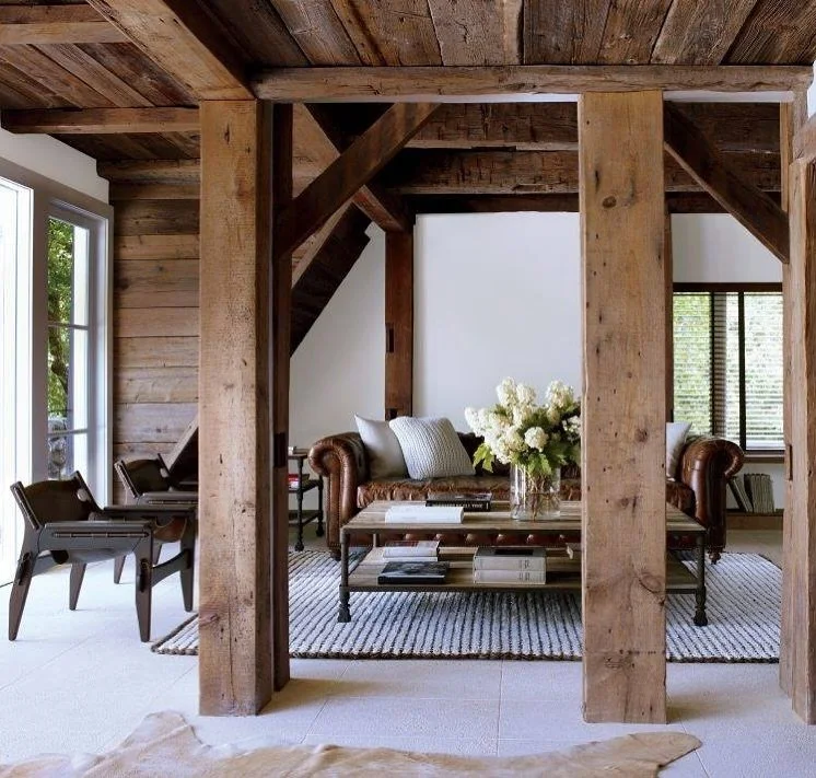 Living room with wooden beams and furniture, including a leather sofa, coffee table, and chairs, with a vase of white flowers on the table.
