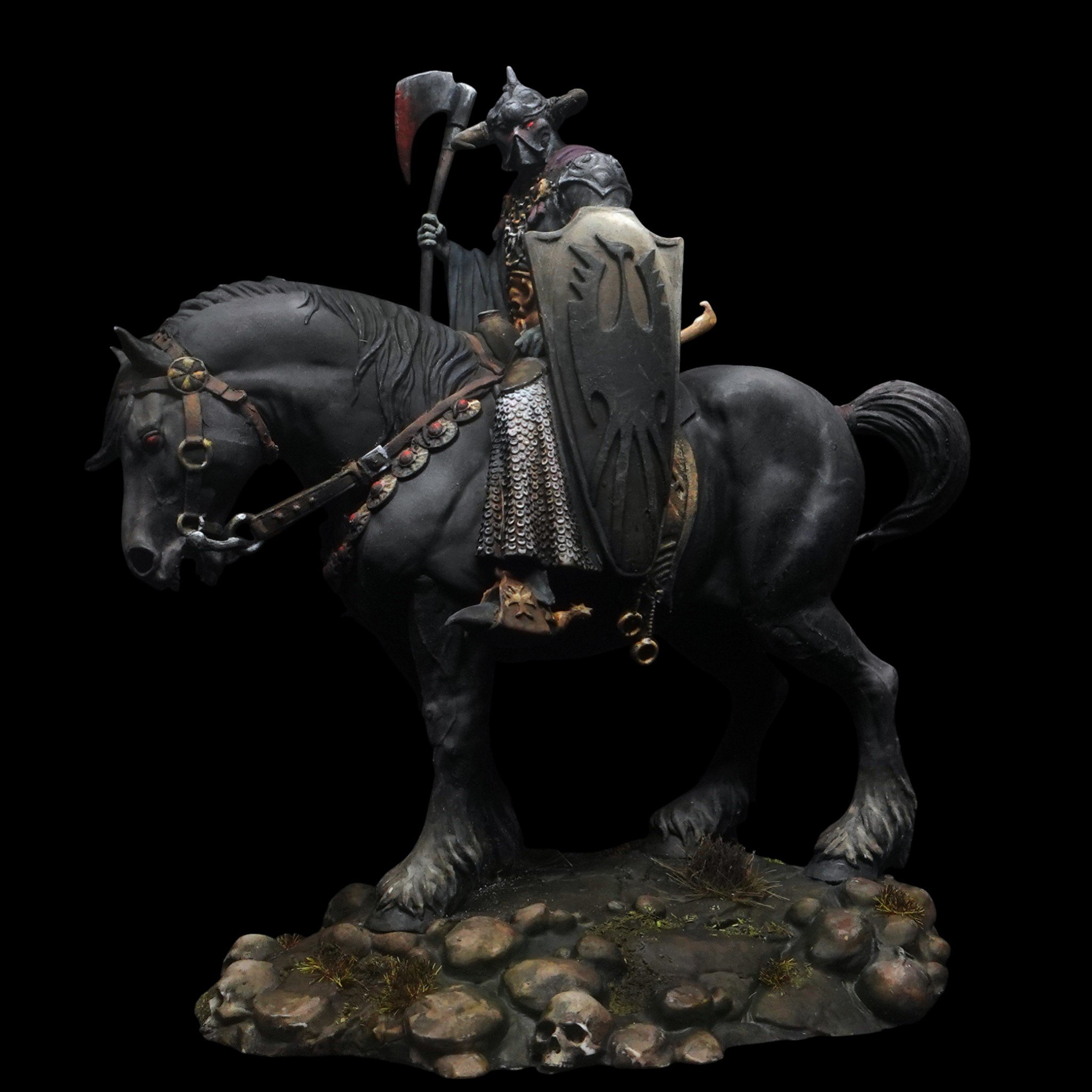 Statue of a Viking warrior riding a horse, wearing a horned helmet, holding an axe, with a shield featuring a dragon or serpent design, on a rocky base with skulls and plants.