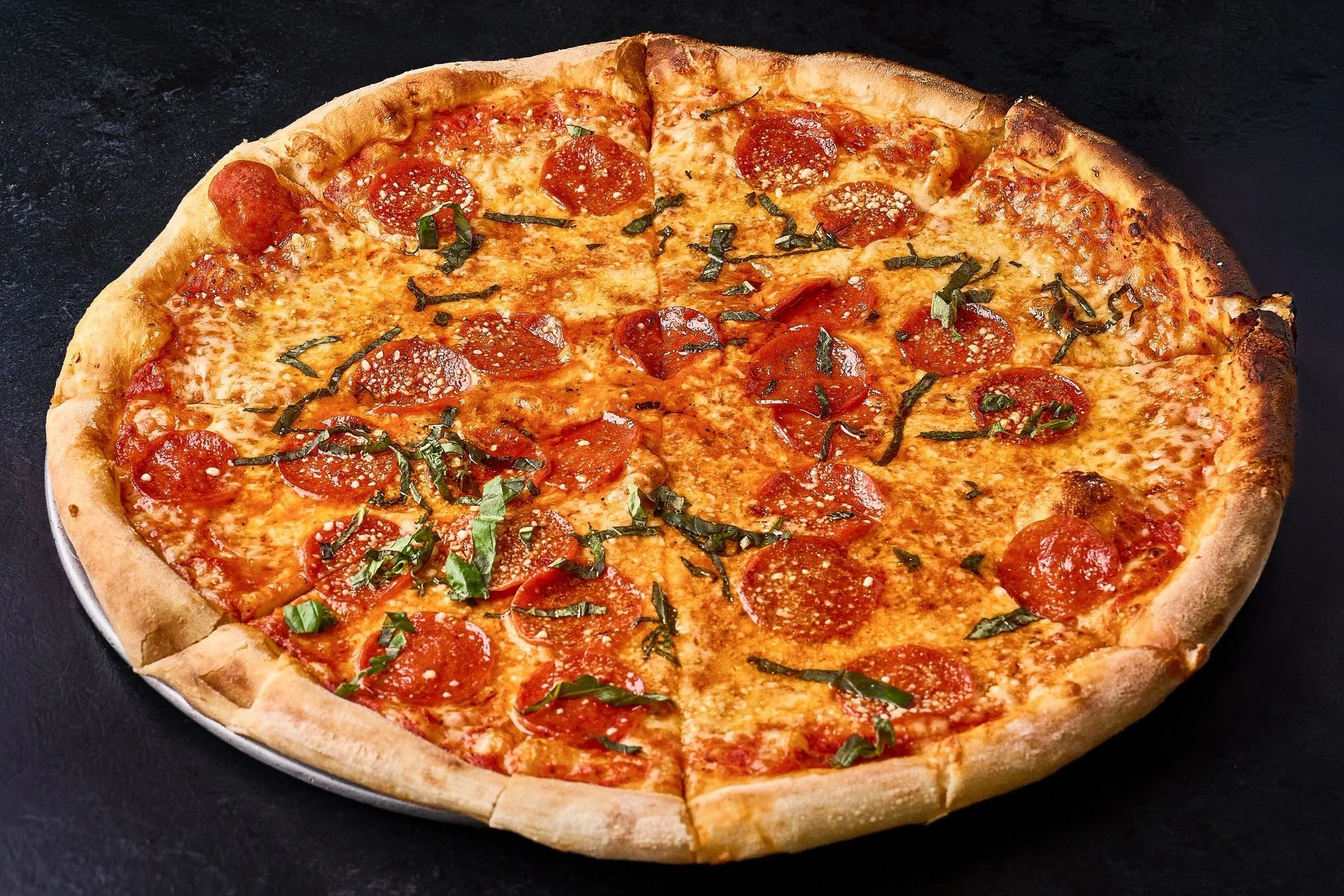 A pepperoni pizza with green herbs on a black surface.