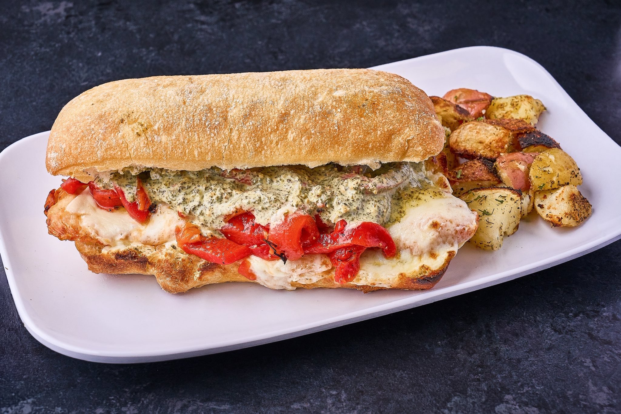 A sandwich on a white plate with roasted potatoes on the side.