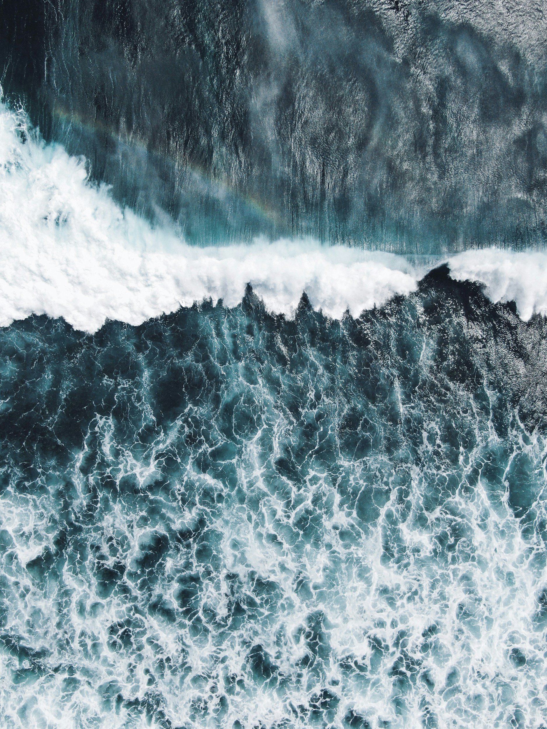 Aerial view of ocean waves crashing, with white foam and deep blue water.