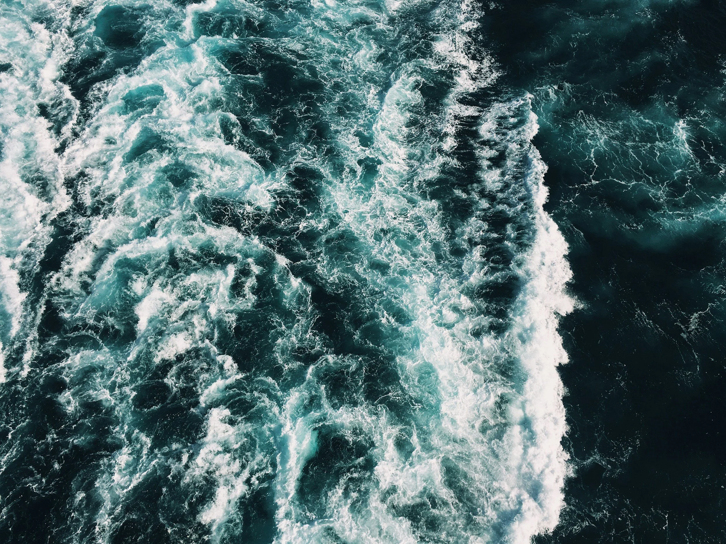 Aerial view of turbulent ocean water with white foam and dark blue waves.